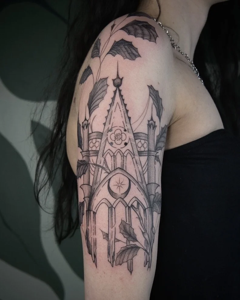 Line art tattoo of a gothic cathedral with pointed arches, a clock, and a moon, surrounded by holly leaves and berries on a person's upper arm and shoulder.