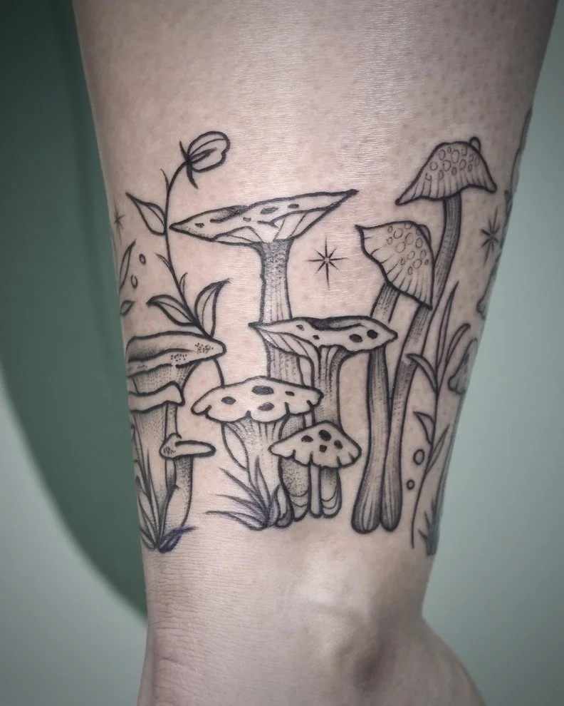 Line art tattoo of mushrooms and plants on skin.