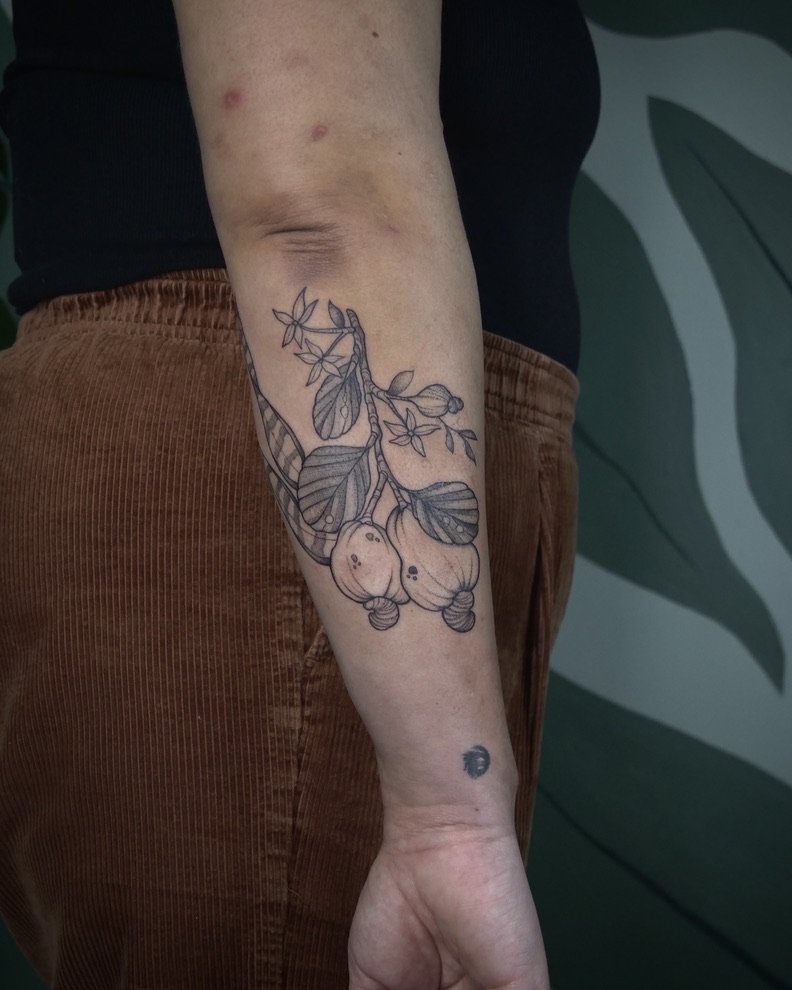 A person's arm with a detailed line drawing tattoo of a branch with pears and leaves.