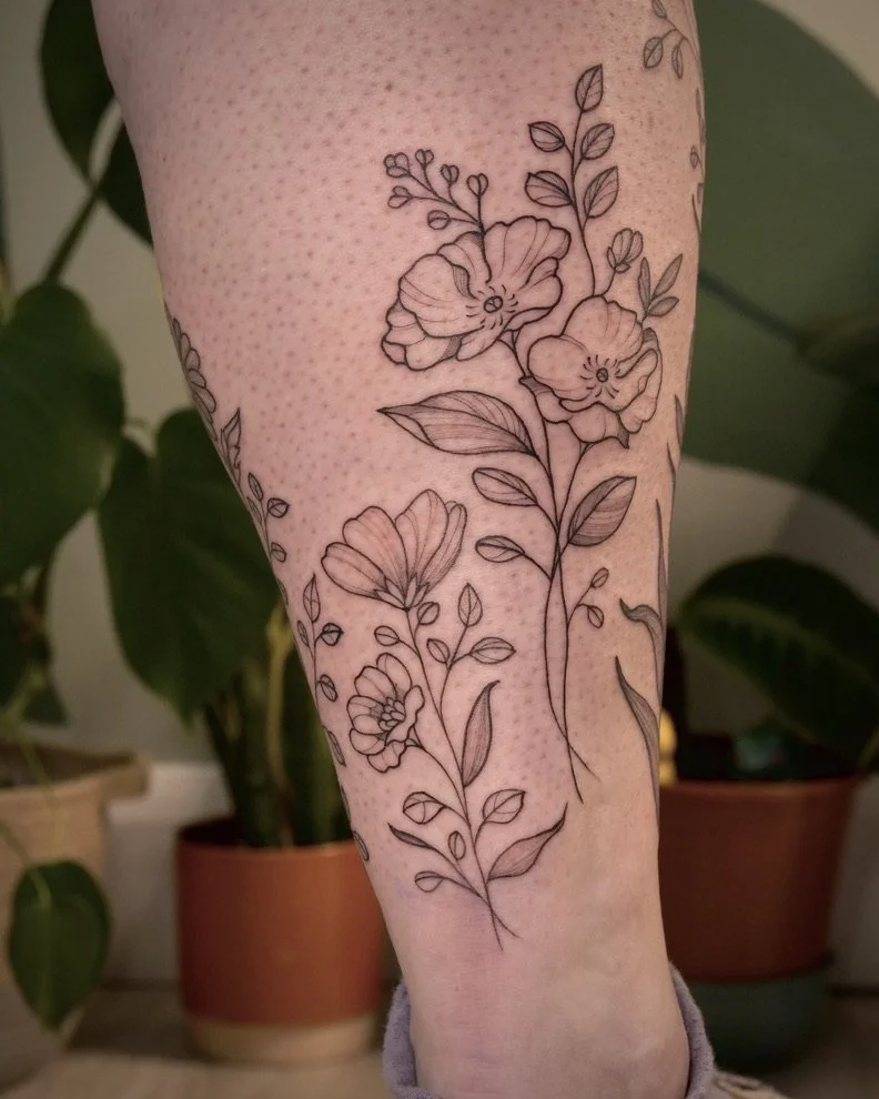 Black line drawing tattoo of flowers and leaves on a person's forearm.