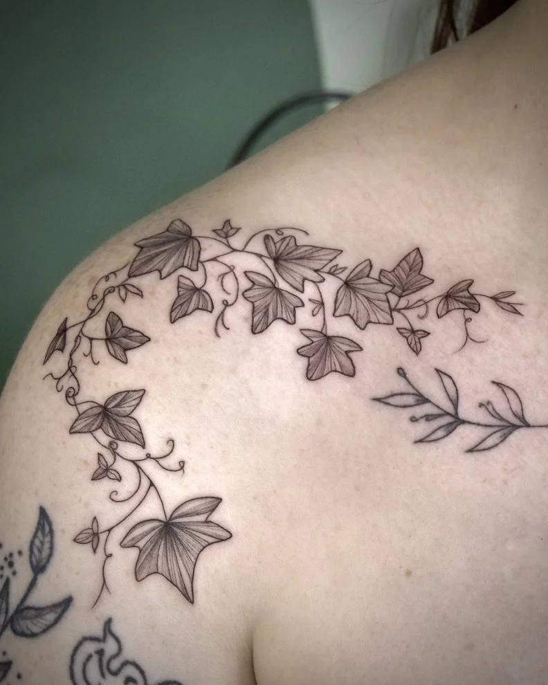 A tattoo of vine, ivy, and leaf designs on a person's shoulder and upper arm.
