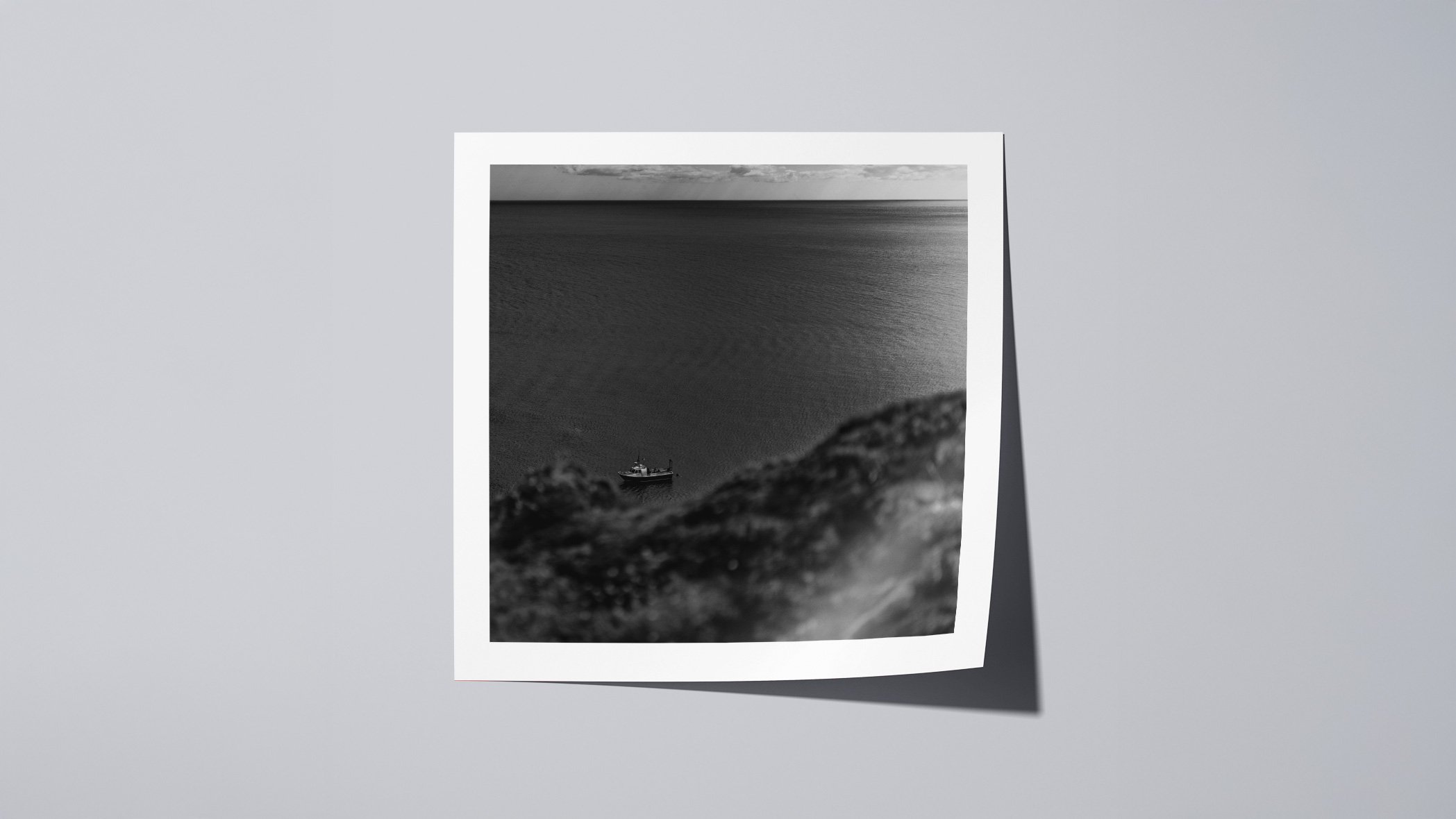 Minimal black and white coastal seascape from St Abbs with a small boat near the horizon under overcast skies.
