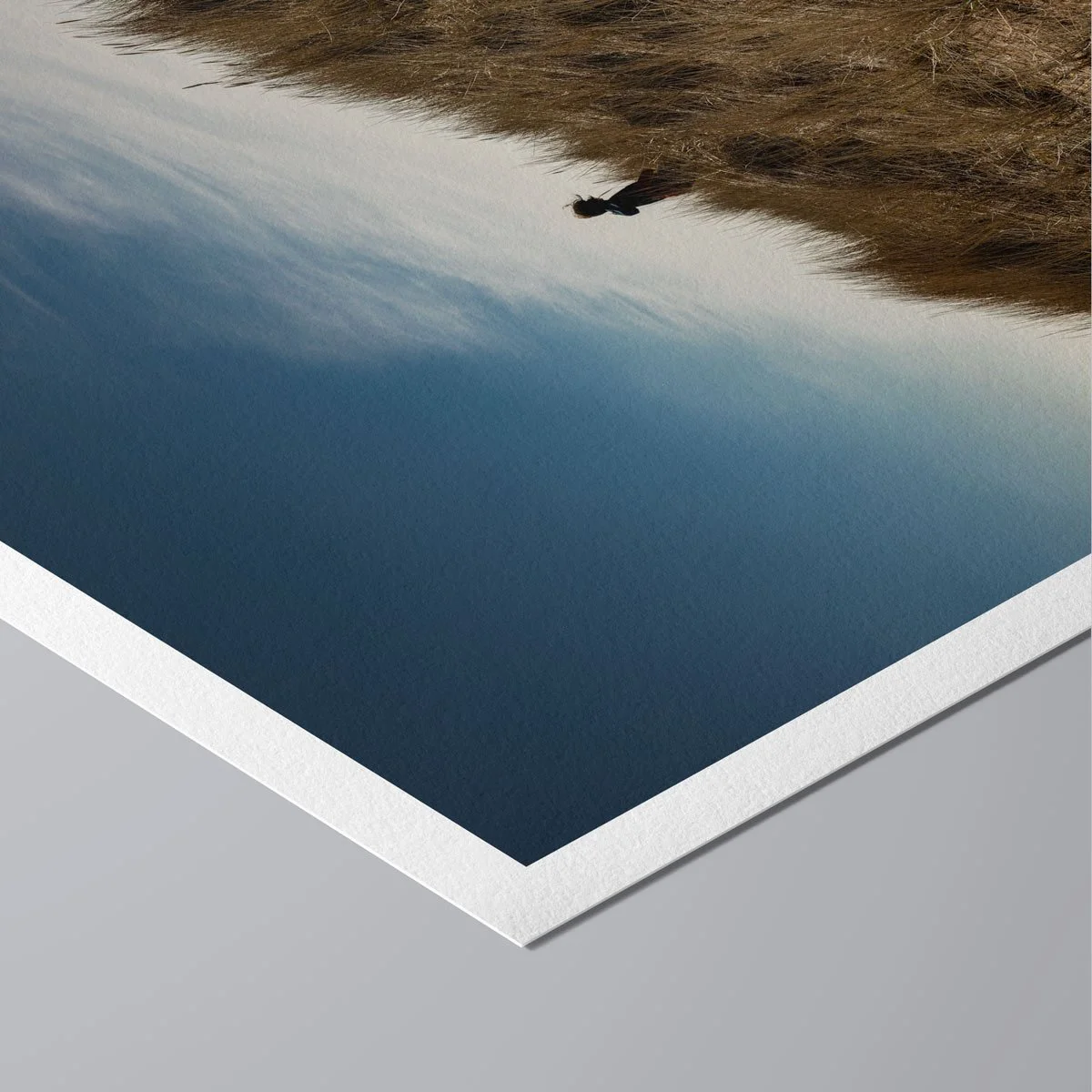 Angled view of a fine art print showing a lone child moving across coastal dunes beneath an open sky.