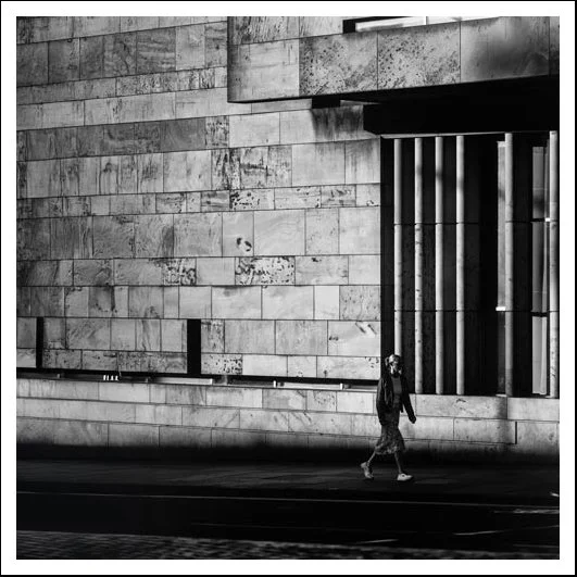 Wide view of modern urban architecture framing a single moving figure in black and white