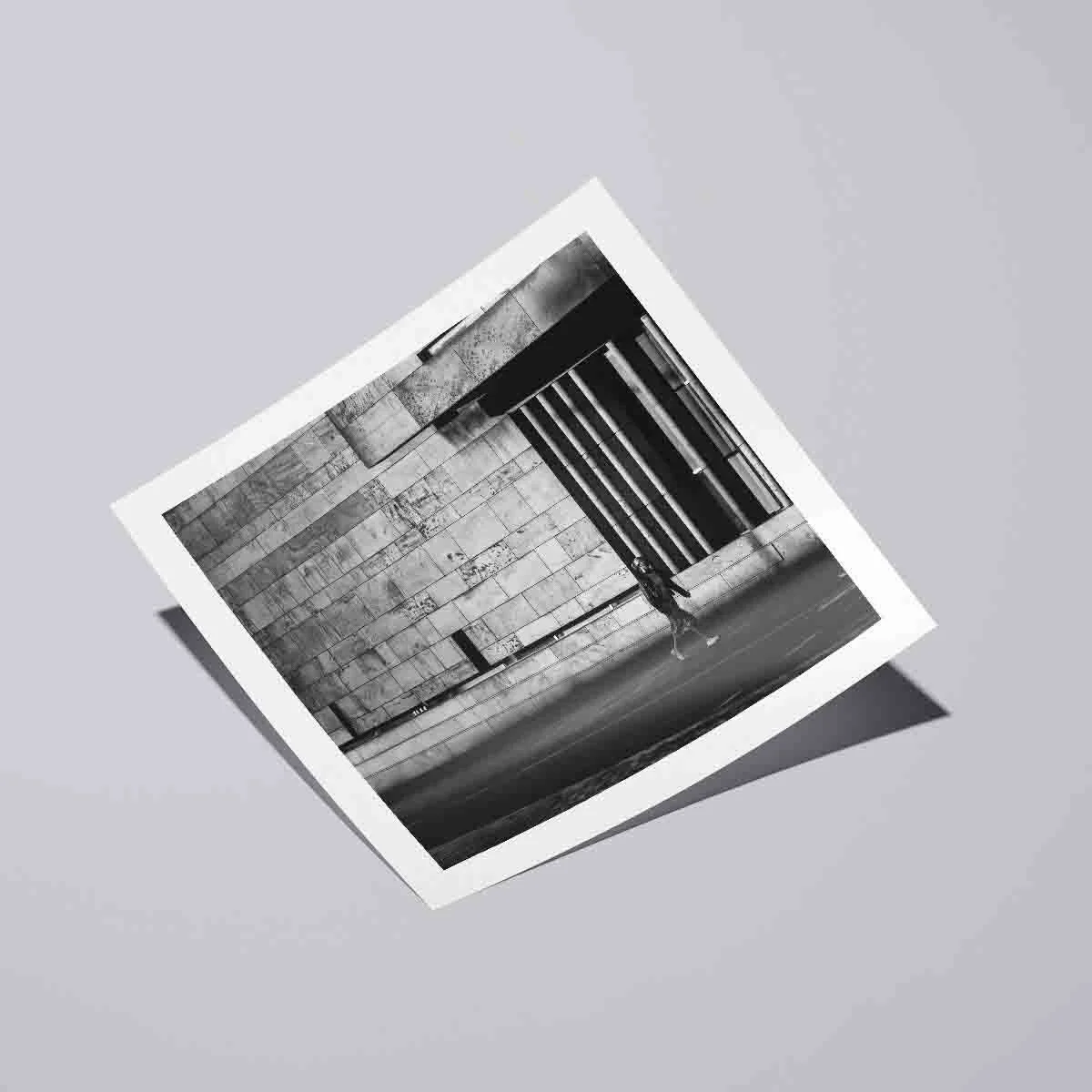 Black and white street photograph showing a solitary figure moving through modern stone architecture