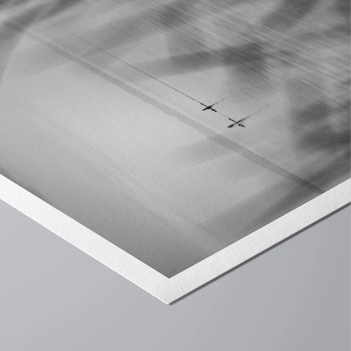 Minimalist monochrome photograph of two paddleboarders on still water seen through out-of-focus grass near the shoreline.