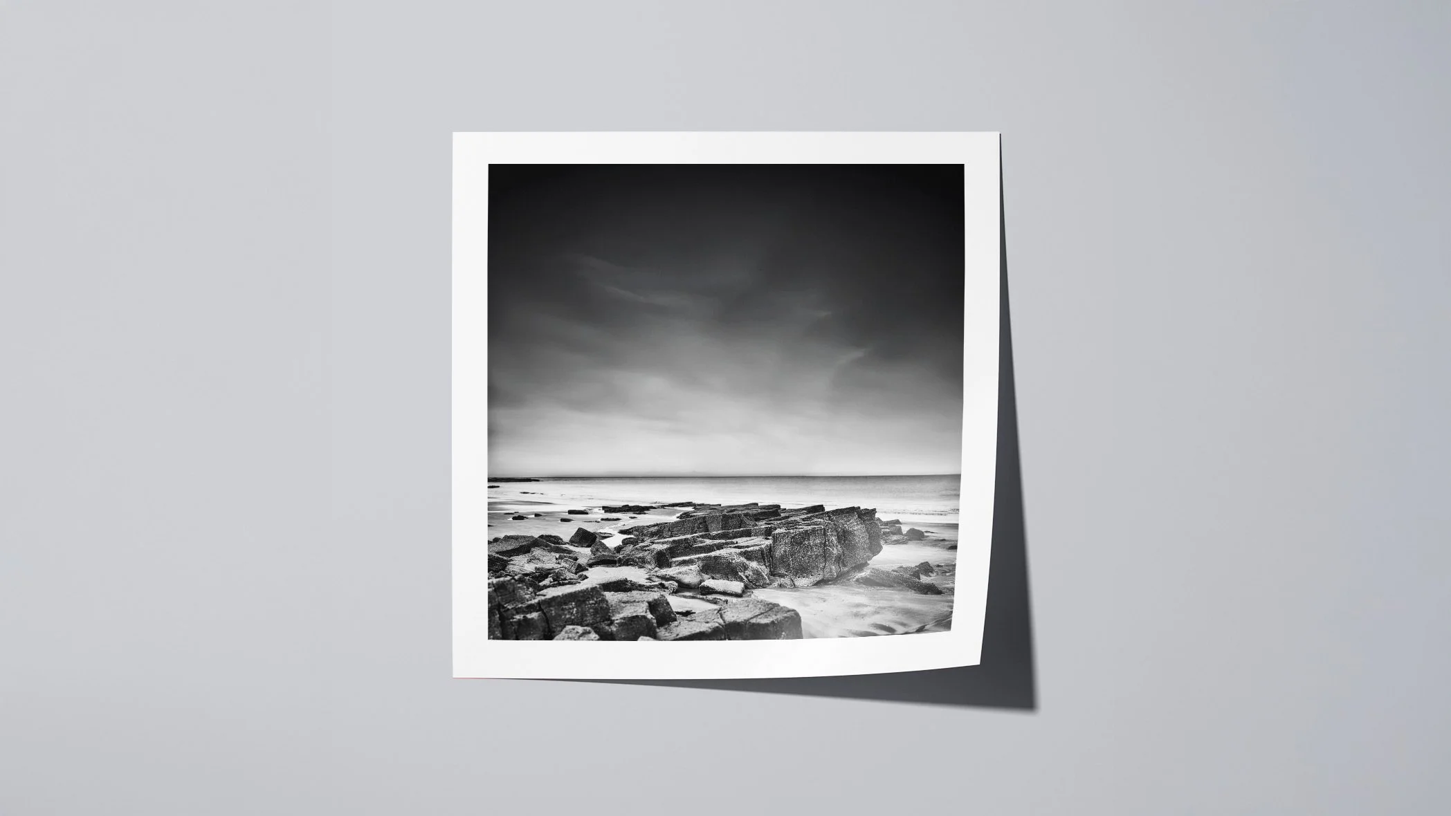 Minimalist square black and white seascape print showing layered rocks on a quiet shoreline.