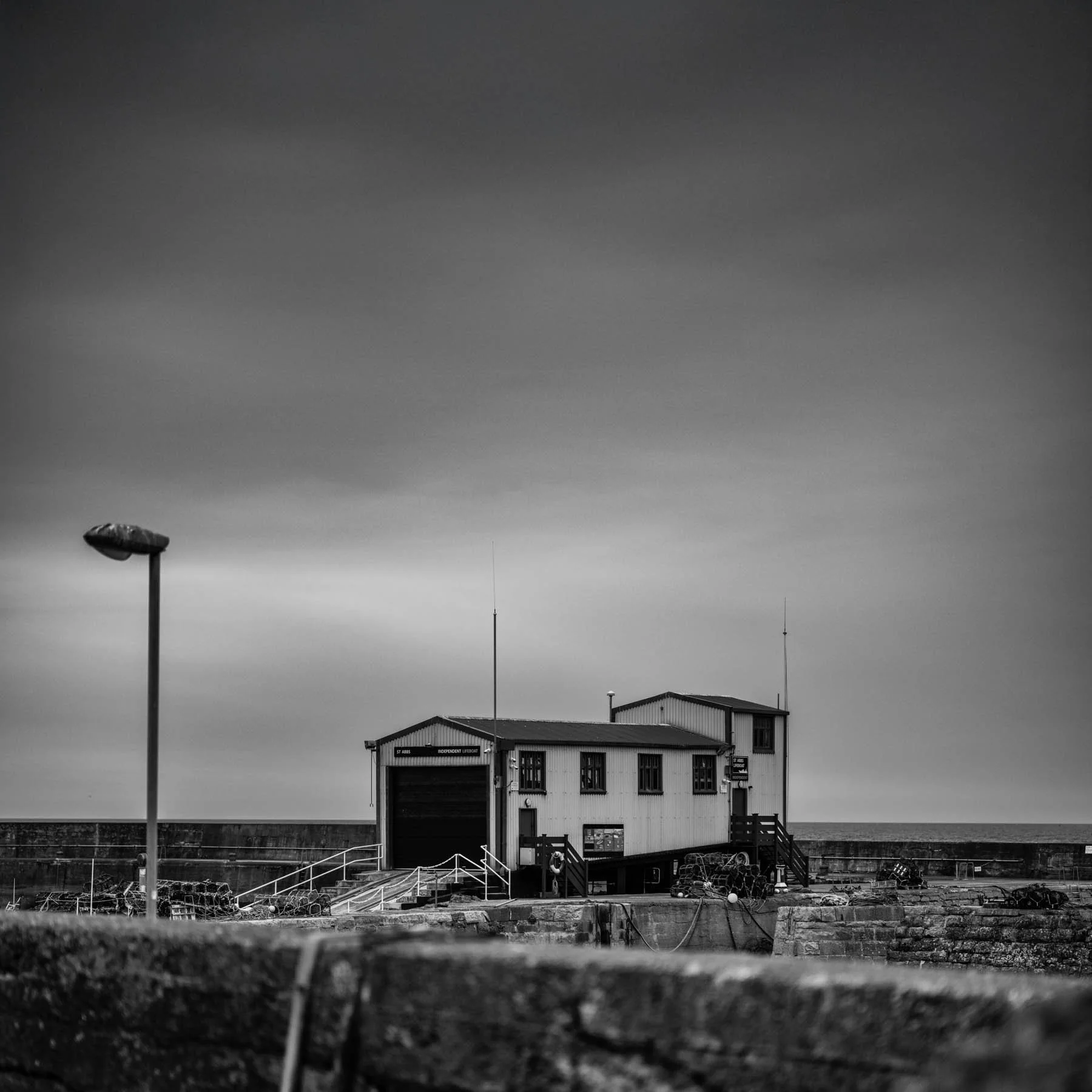 A black and white architectural image of a harbor station with strong linear forms and overcast skies, emphasizing functional design in a minimal palette.