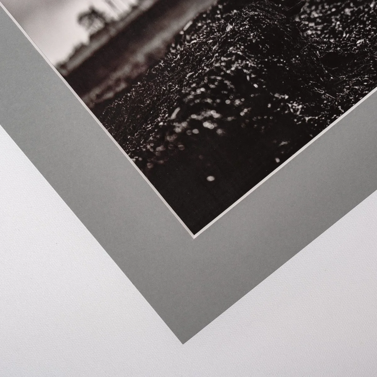 Top corner detail of mounted black and white coastal photograph, minimal fine art presentation with grey mat board