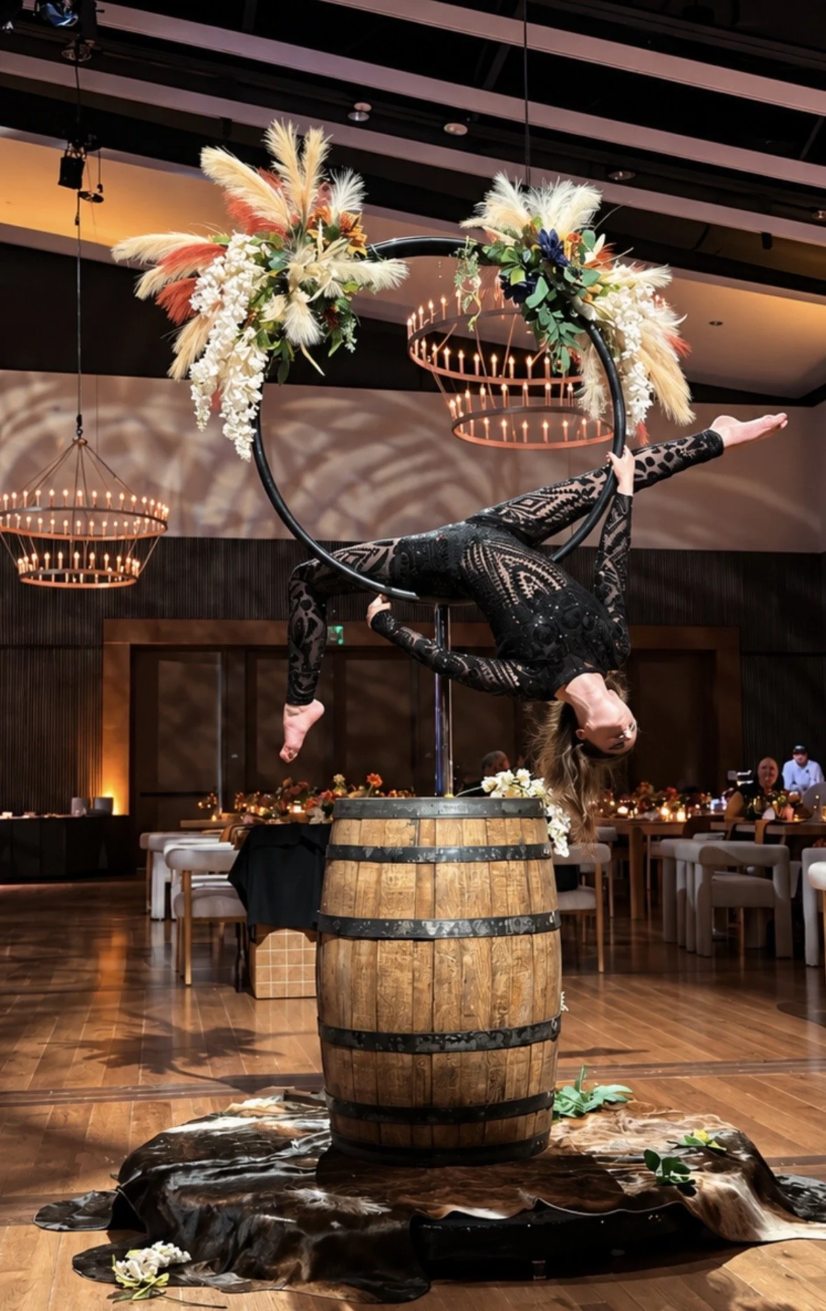Aerialist in a black lace bodysuit inverted in an aerial hoop topped with pampas and florals, mounted on a whiskey barrel in an event ballroom at the Country Music Hall of Fame