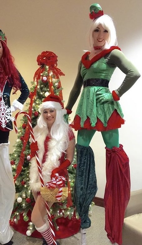 Christmas elf stilt walkers and holiday performers by a Christmas tree