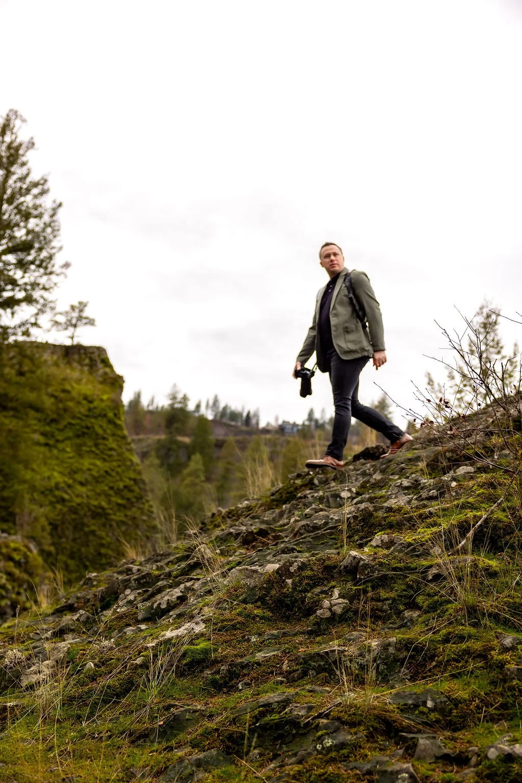 Photographer walking down a jagged rock decline with camera and looking off into the distance