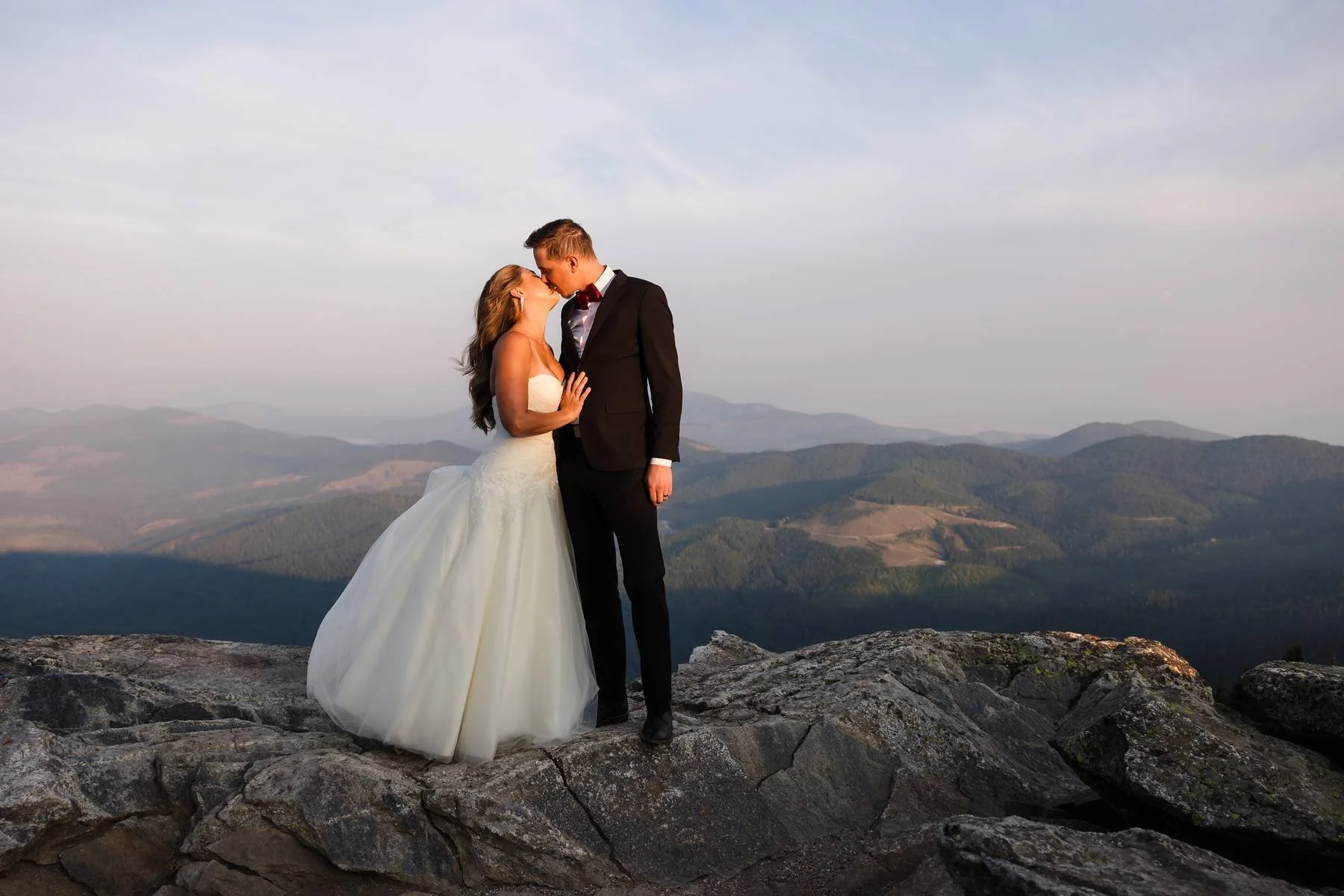 Bride and Groom kissing at the top of Mt. Spokane with a view of the hills behind them.