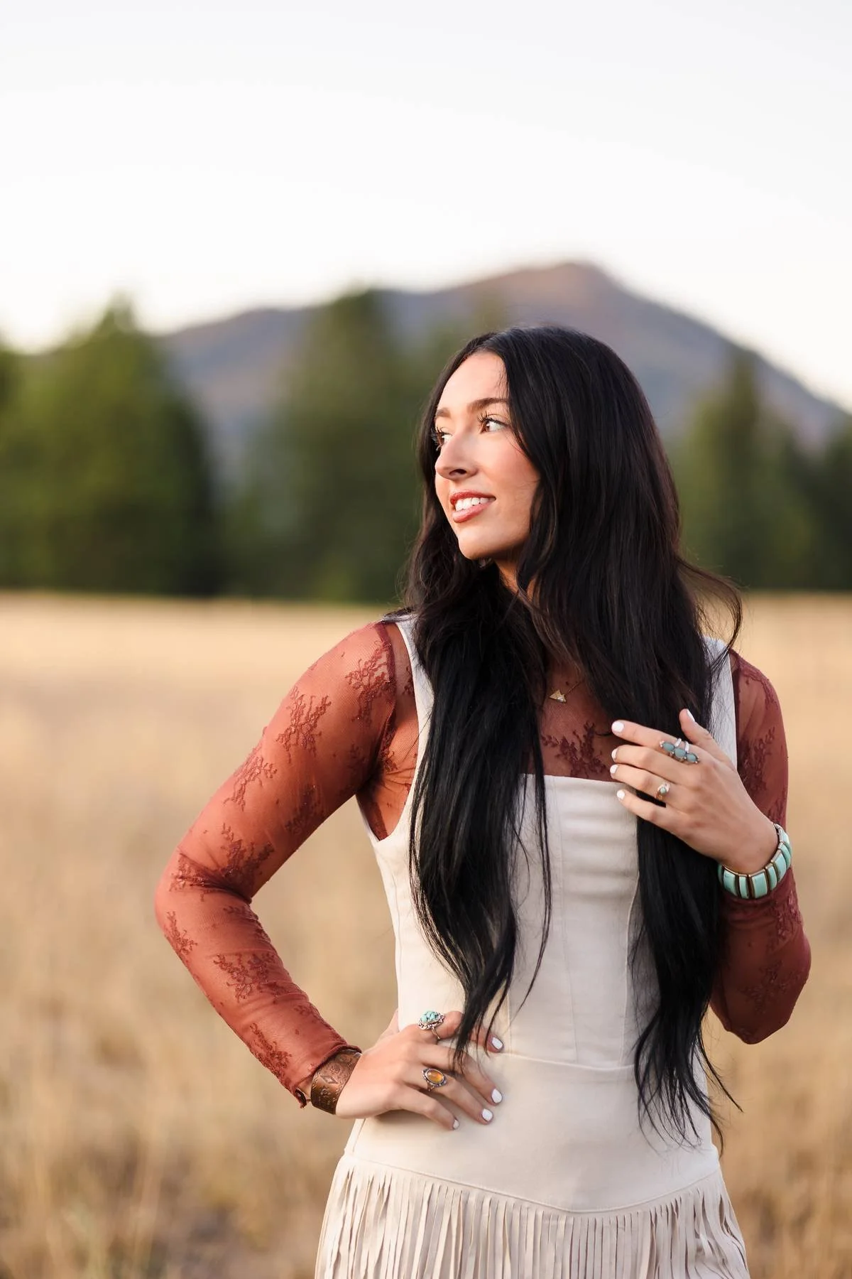 Girl in a western style outfit standing in a field of golden grass with a mountain in the background