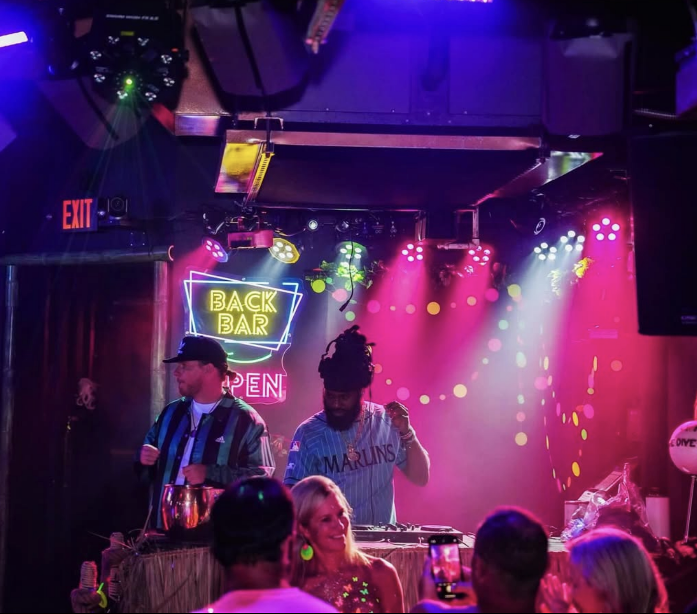 DJ performing at a lively nightclub with pink and purple lighting, neon