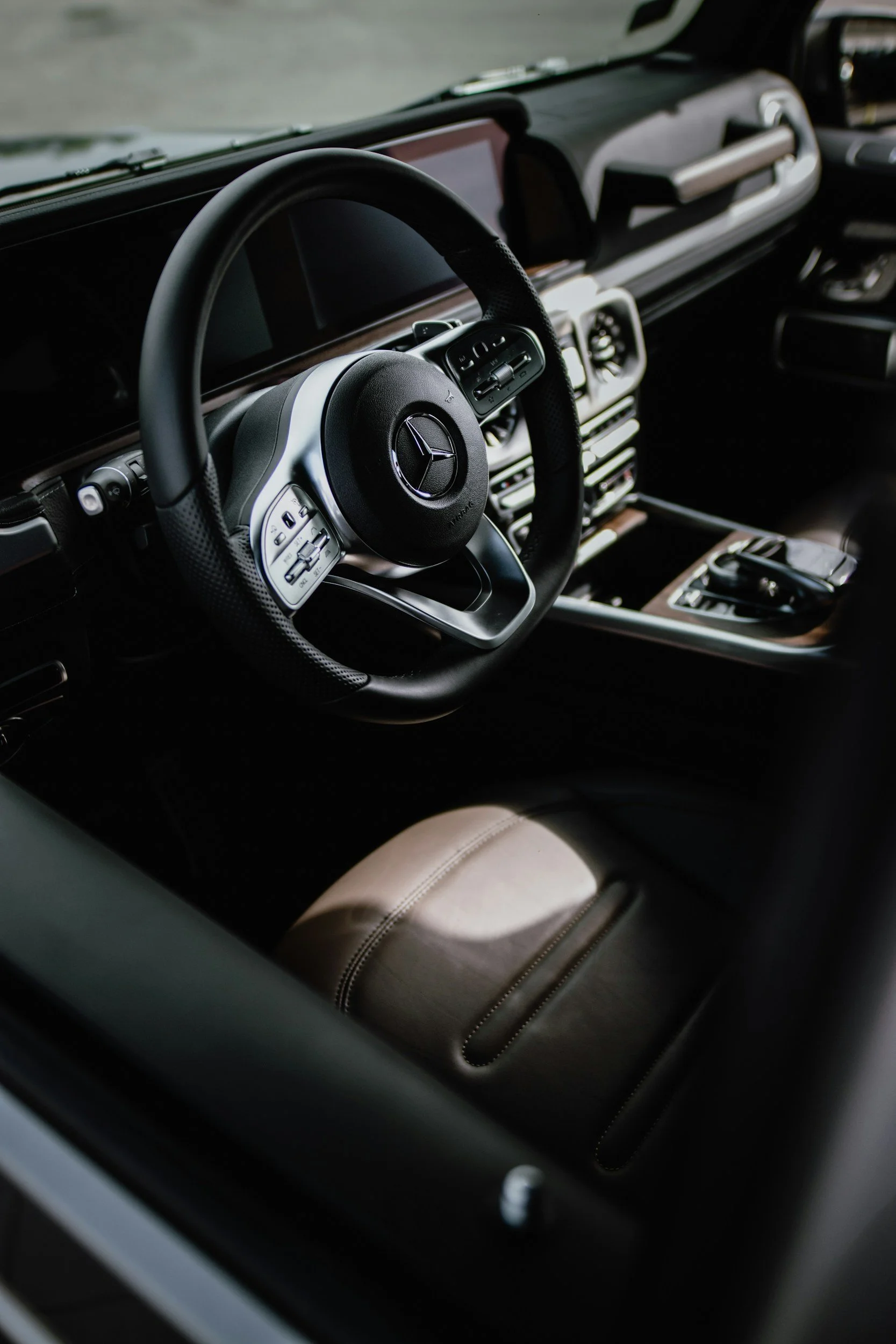Interior of a luxury car, showing a Mercedes-Benz steering wheel, dashboard, and center console with gear shift.