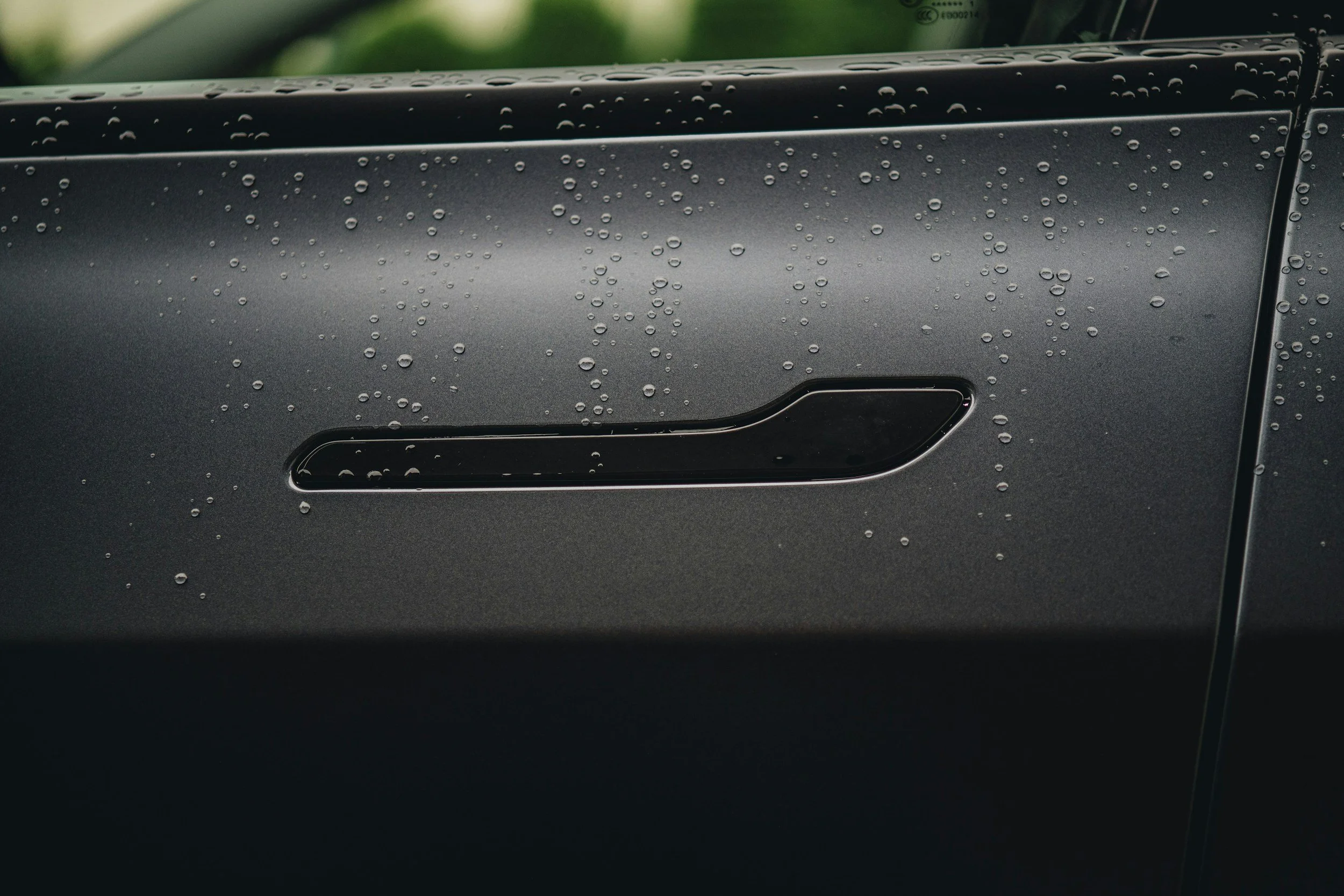 Close-up of a car door handle with water droplets on a dark gray vehicle