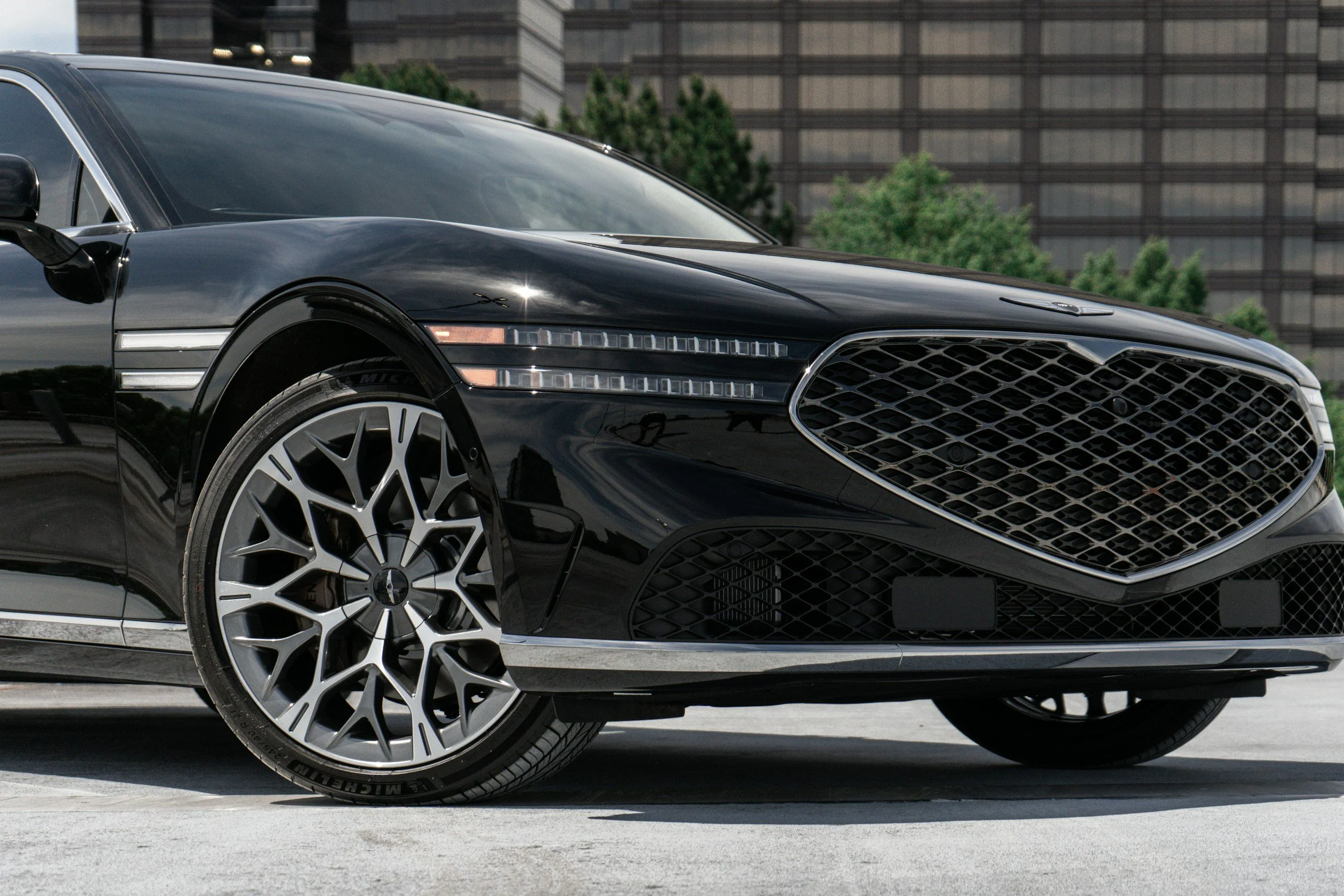 Close-up of a black luxury car's front side, showing the front wheel, grille, and part of the hood.