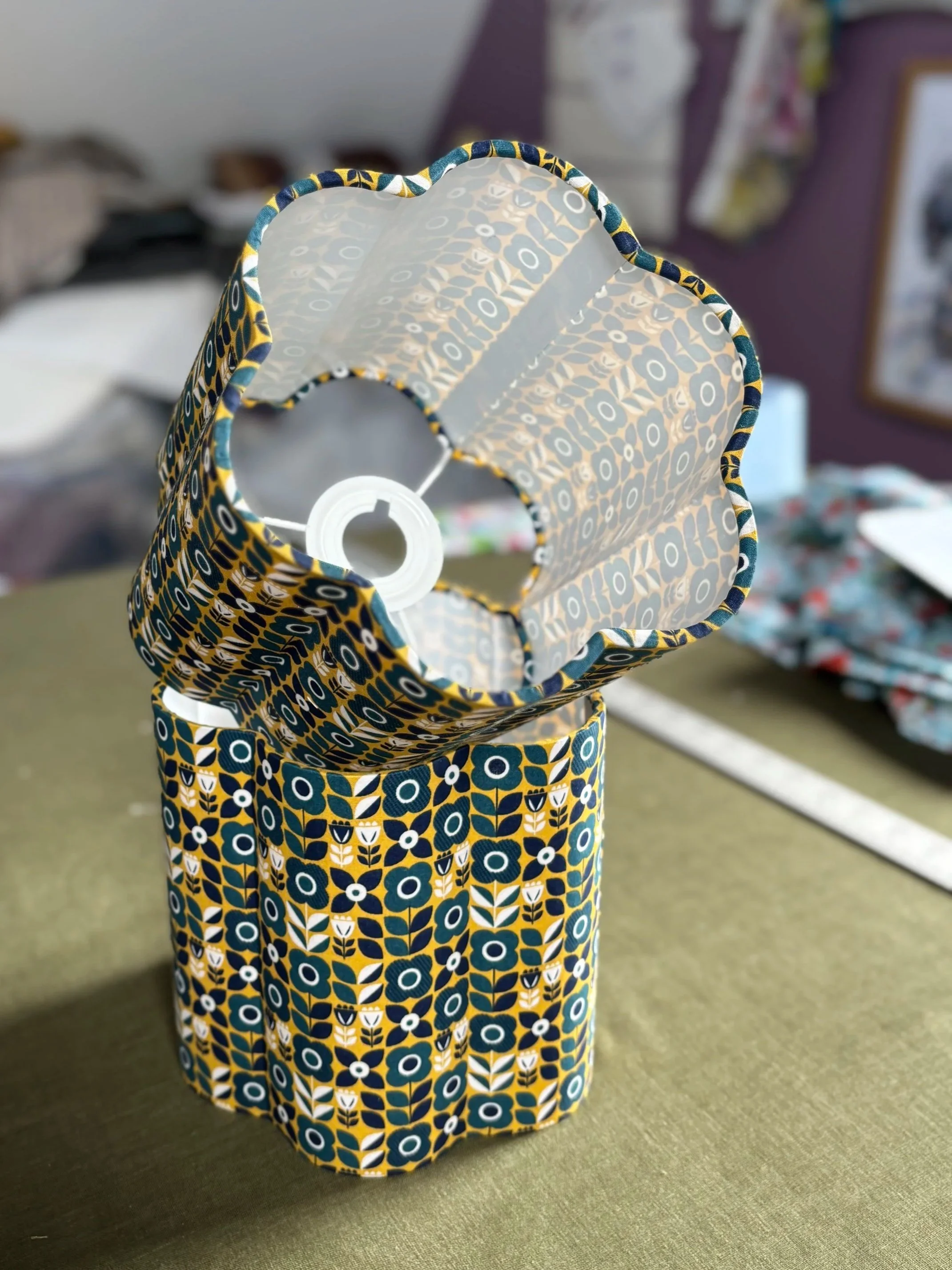 A small 20cm scallop shaped lampshade with a colourful geometric pattern, showing its interior and a light bulb socket inside, placed on a flat surface. suitable for bedside table lamp bases.