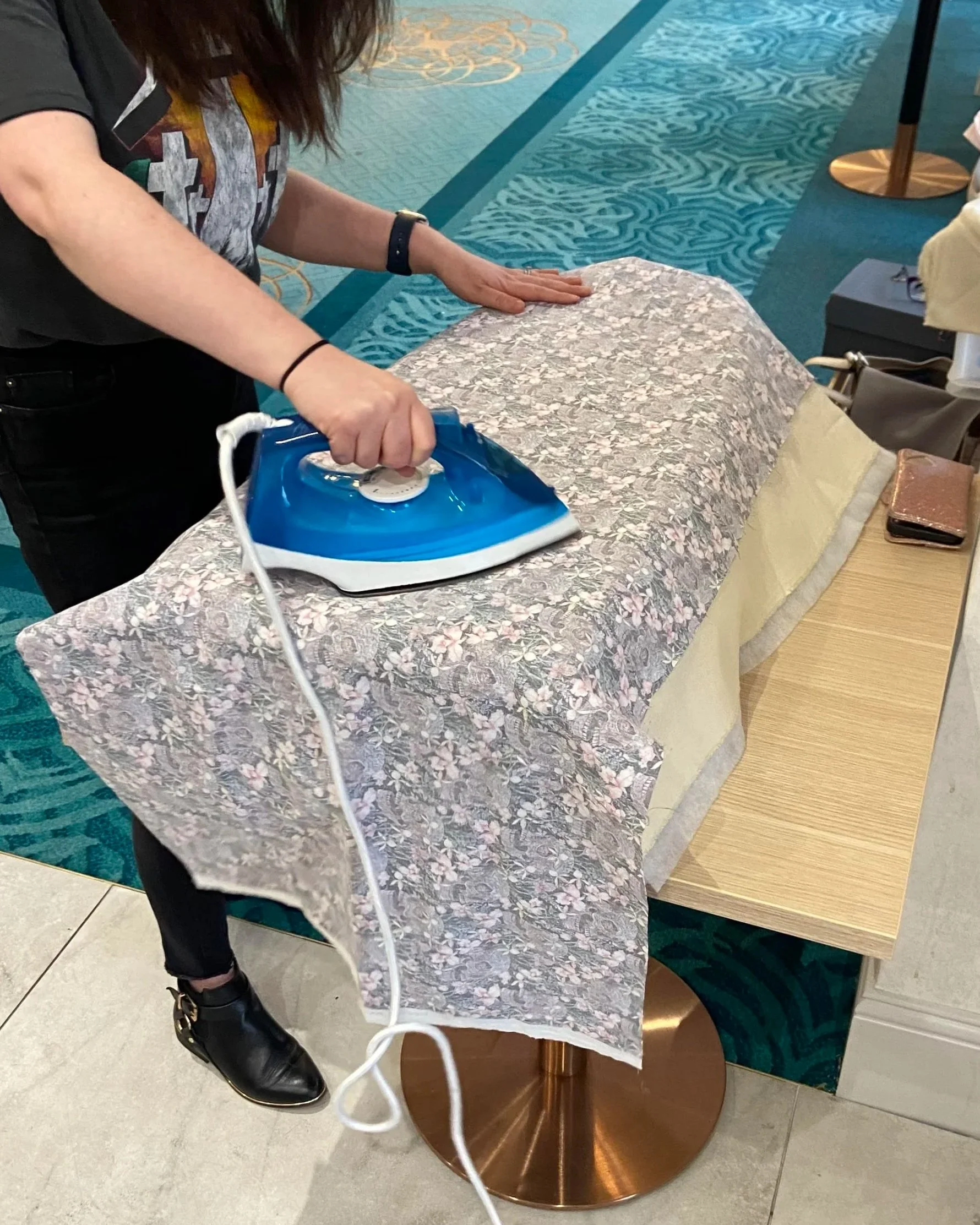Person ironing a floral fabric tablecloth at a lampshade making workshop setting