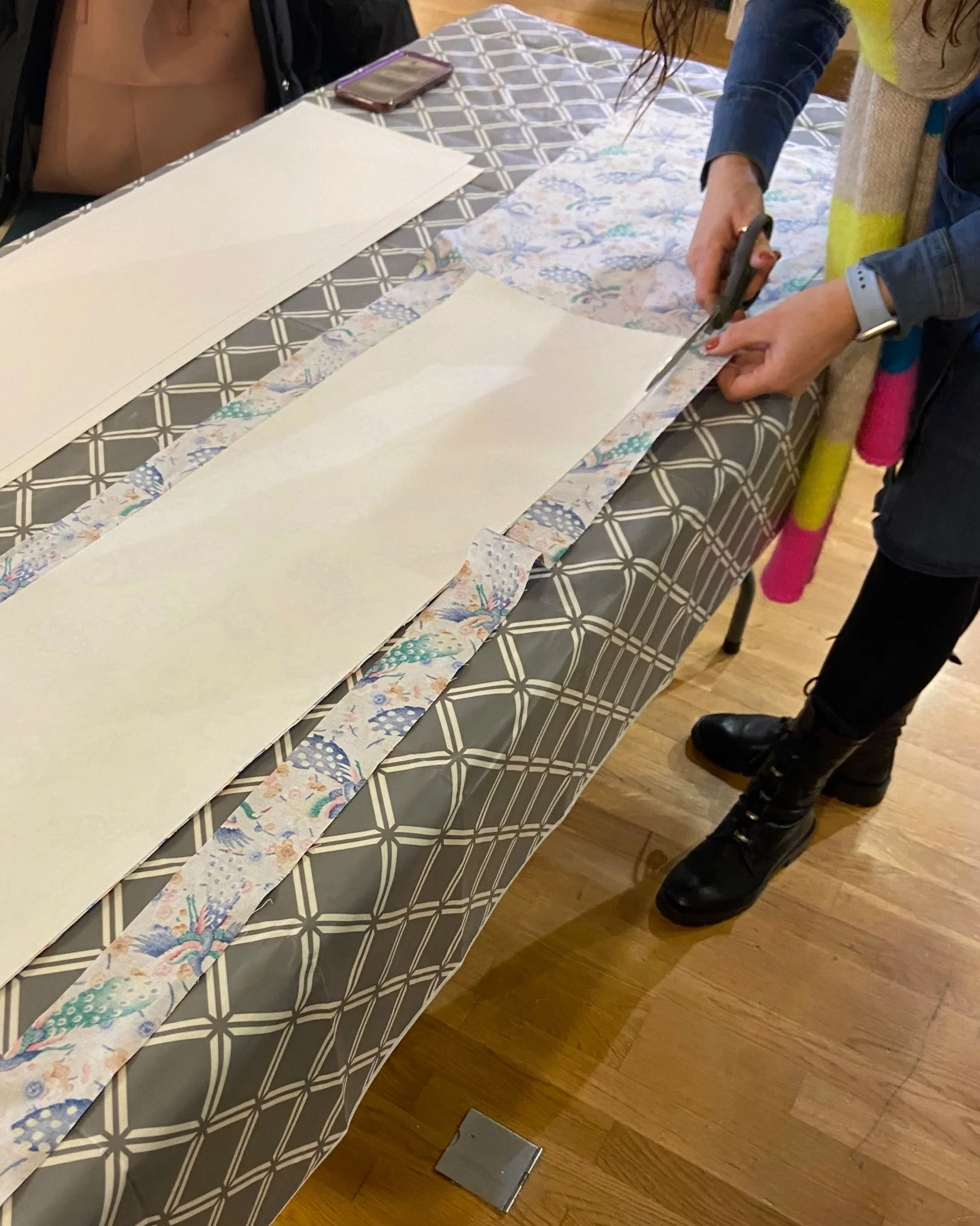 Person cutting fabric with scissors on a table while attending a lampshade making workshop
