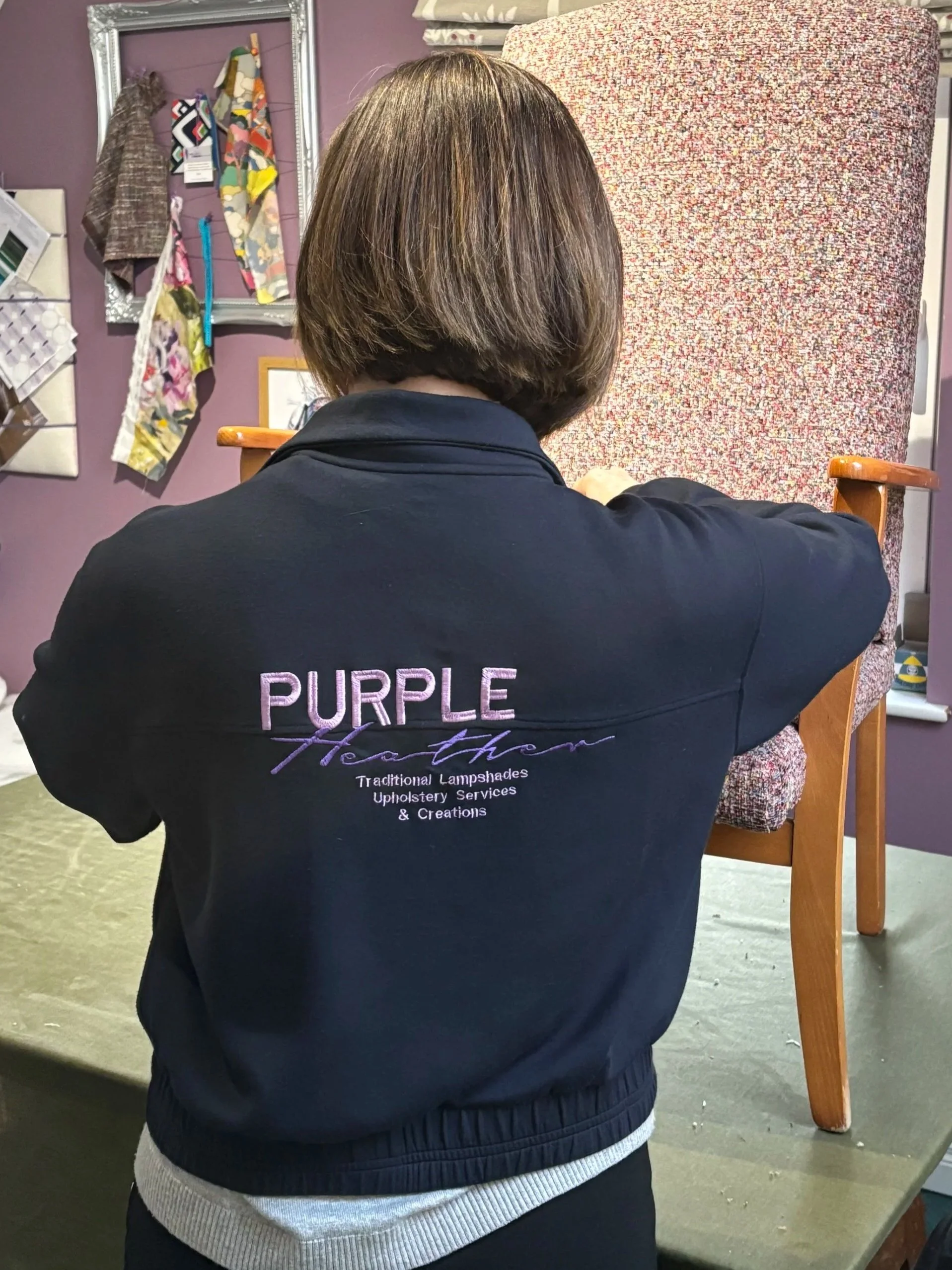 Heather owner of Purple Heather Upholstery and Creation in logo branded jacket in her workshop.