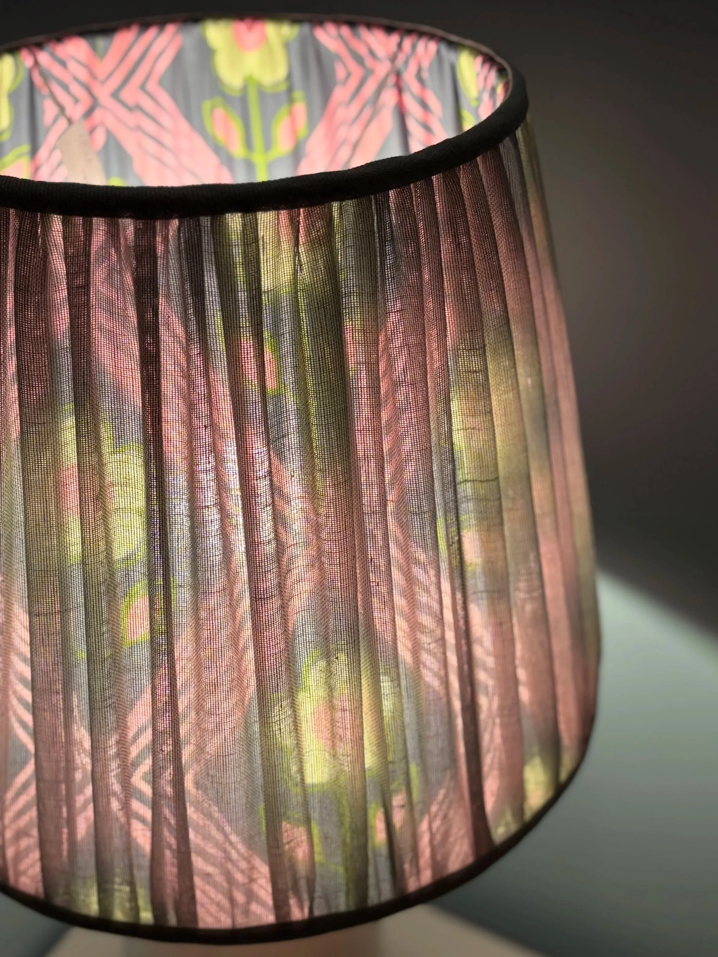 Close-up of a colourful French drum shaped lampshade with a floral lining and geometric pattern, illuminated from within, casting a soft glow. two layers of fabric on this hand stitched bespoke lampshade
