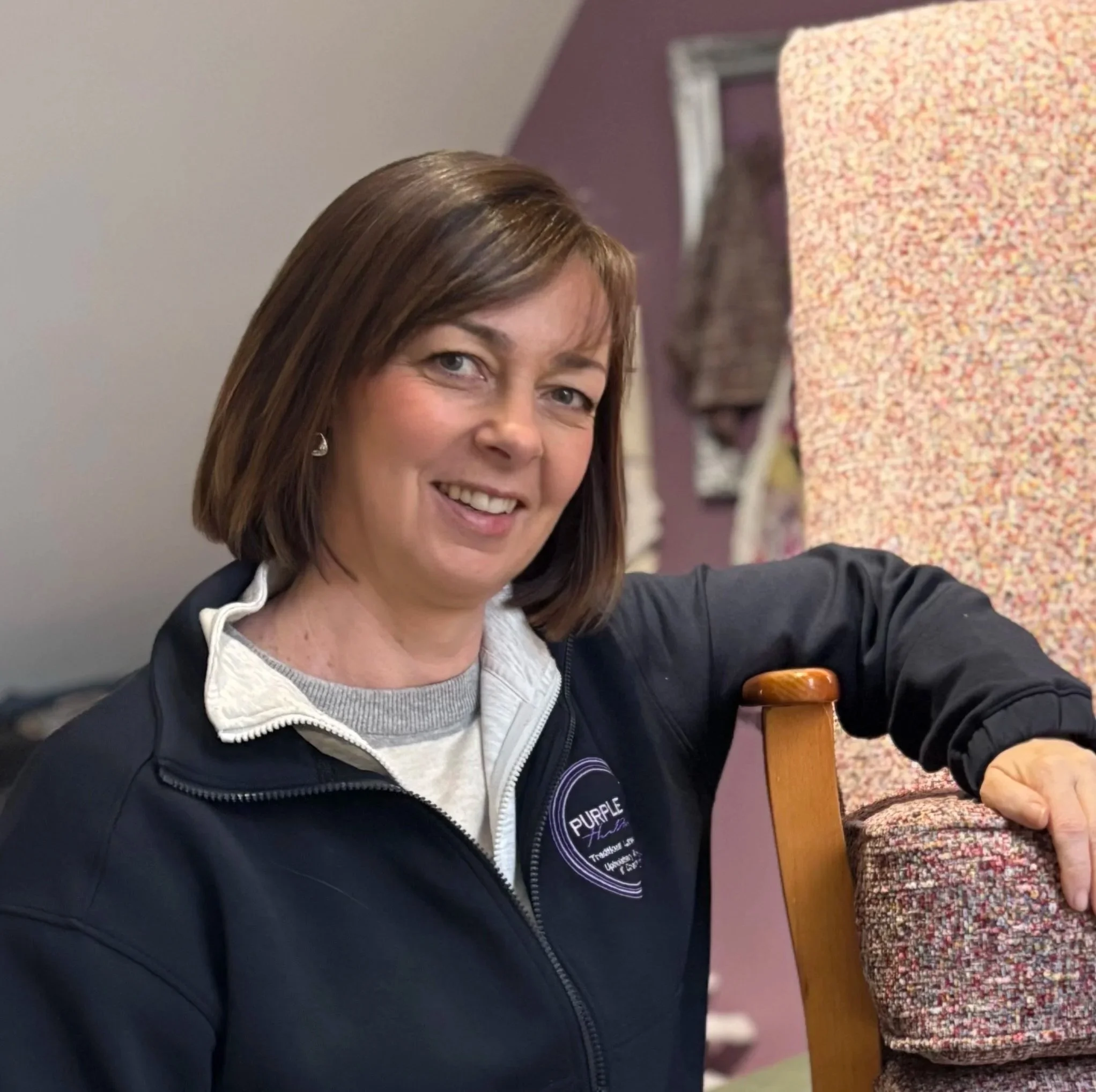 Purple Heather female upholsterer based in Dromore County Down Northern Ireland. Pictured in her workshop wearing a navy jacket with Purple Heather Upholstery and Creations logo