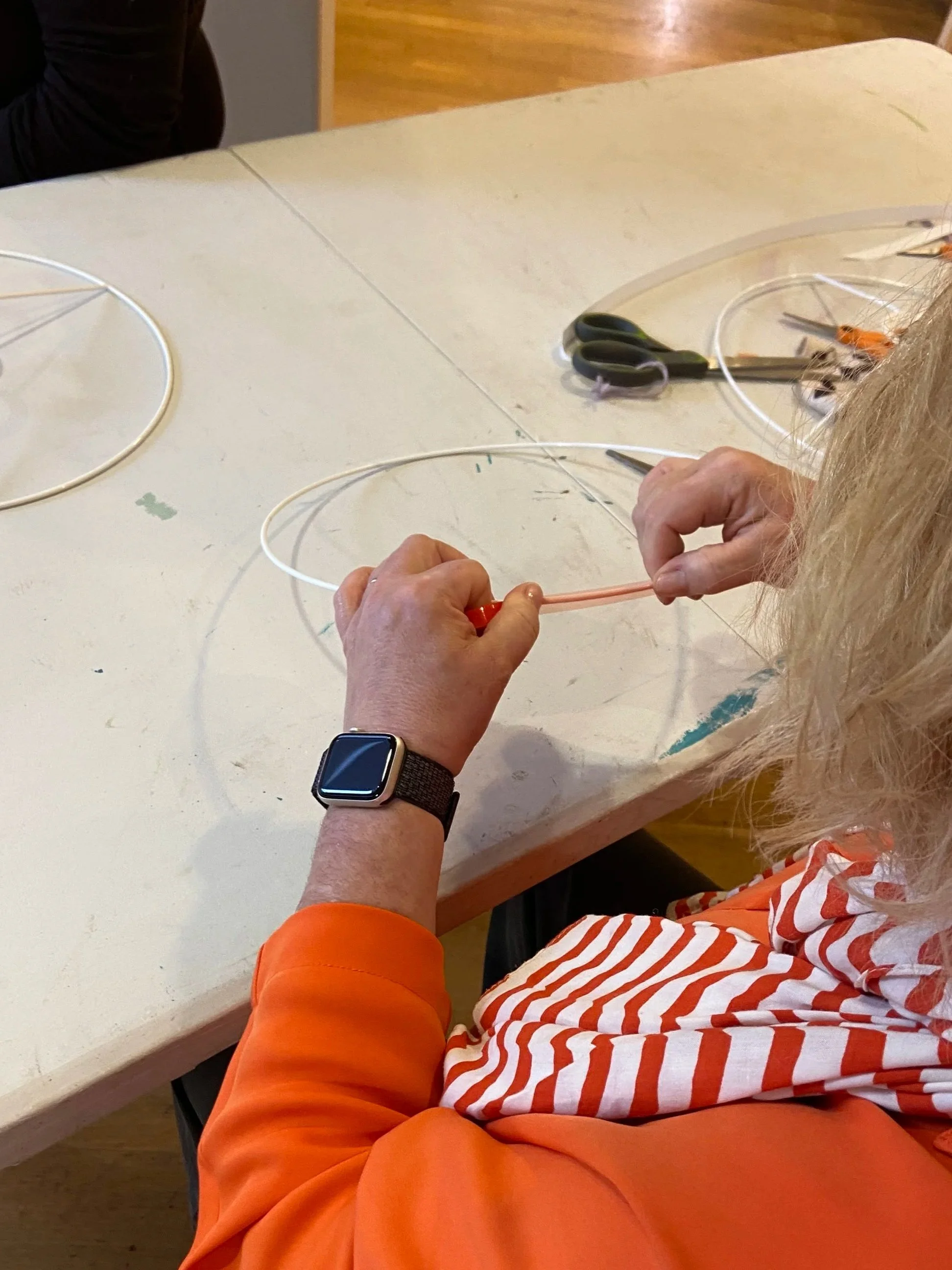 Person sitting at a table adding tape to a lampshade rings, working in a lampshade making workshop