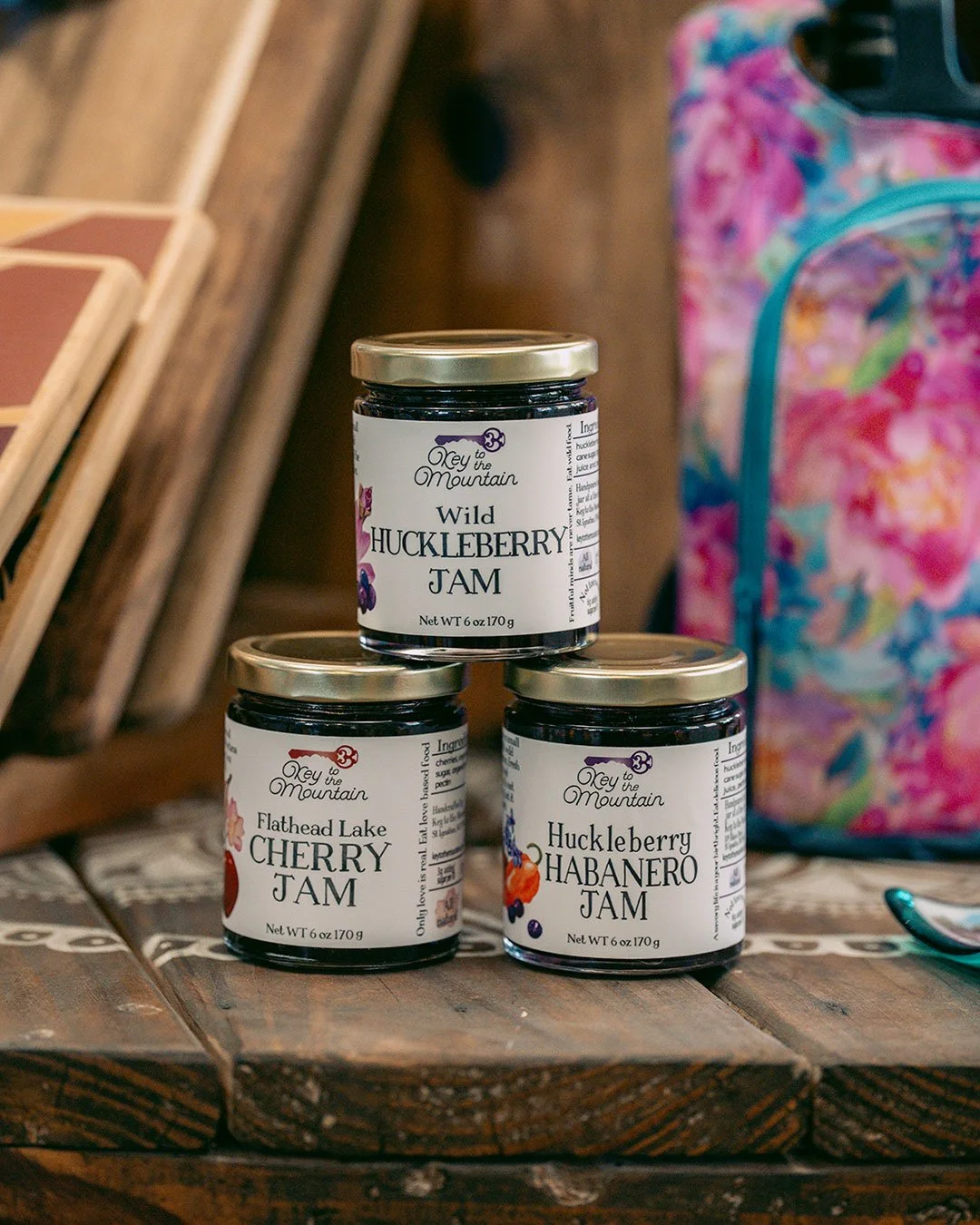 Three jars of Key to the Mountains huckleberry jams sit in a pyramid in front of colorful product in the gift shop.