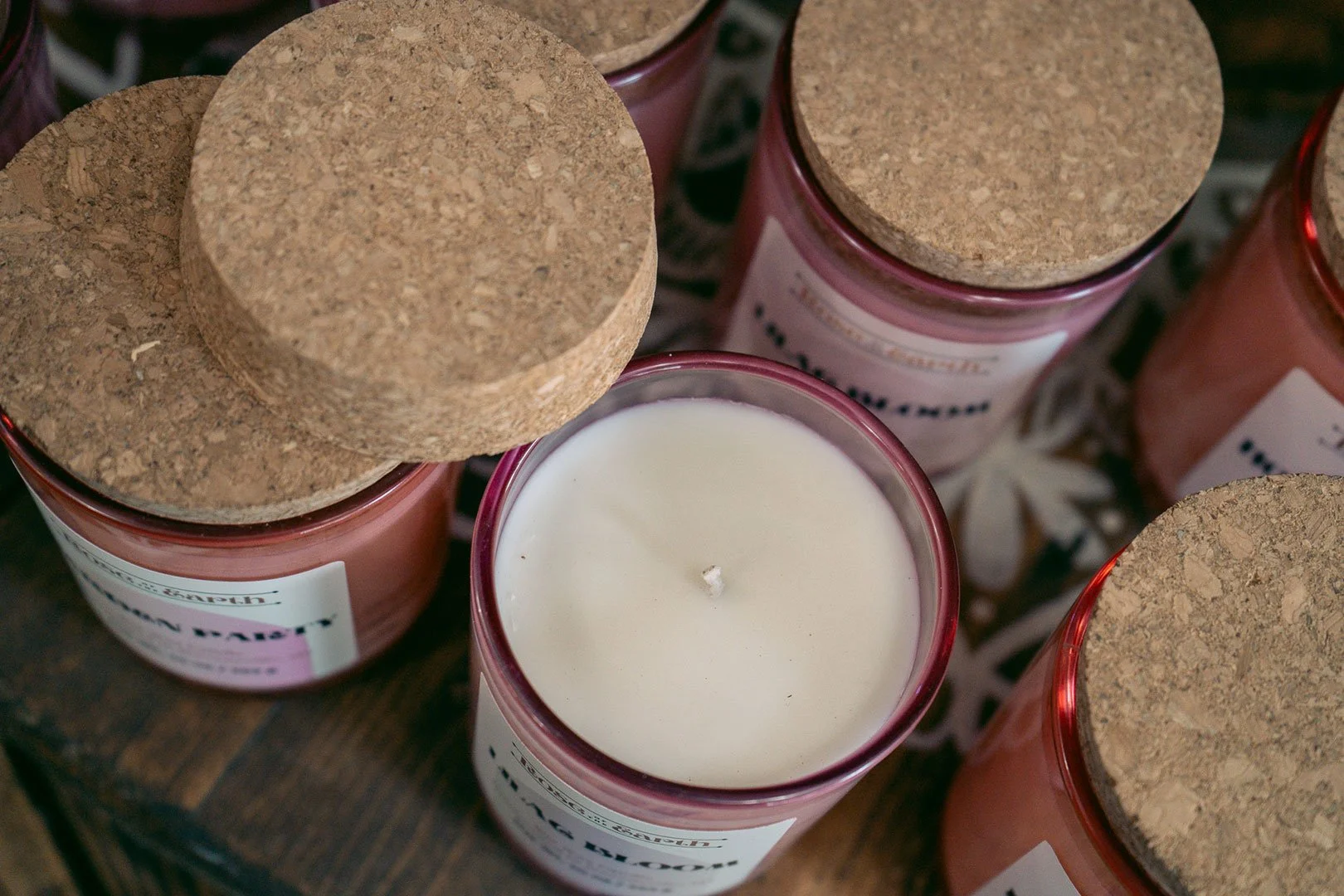 A candle in a pink jar sits open amongst several other hand-poured candles from Rose of the Earth.