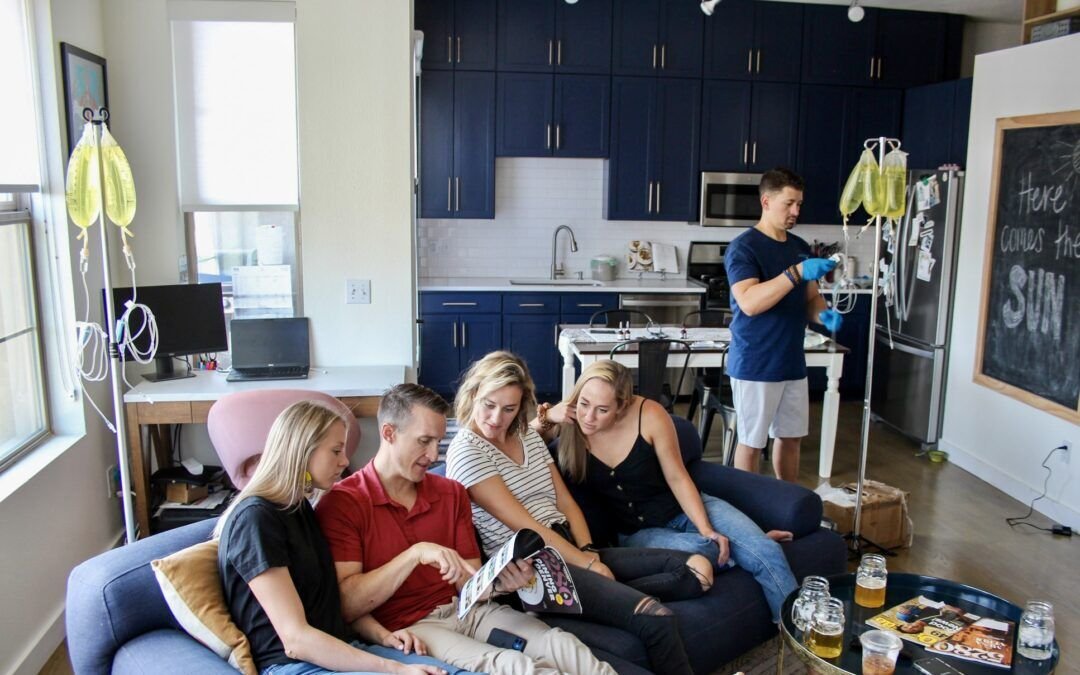 Group of friends relaxing on a couch at home while a clinician prepares IV drips for a mobile IV therapy event