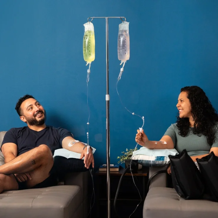 Two IV drip bags hanging from an IV stand against a blue wall during IV hydration therapy