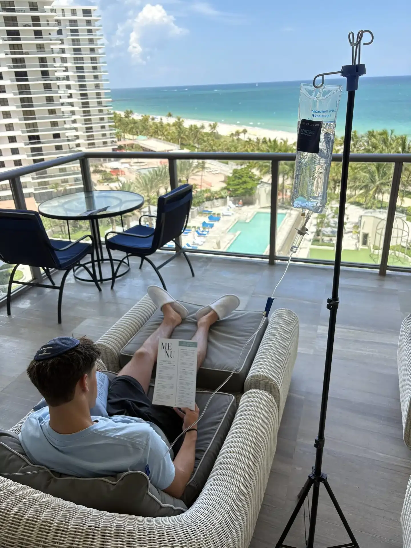 Guest relaxing on a hotel balcony with an ocean view while receiving mobile IV therapy