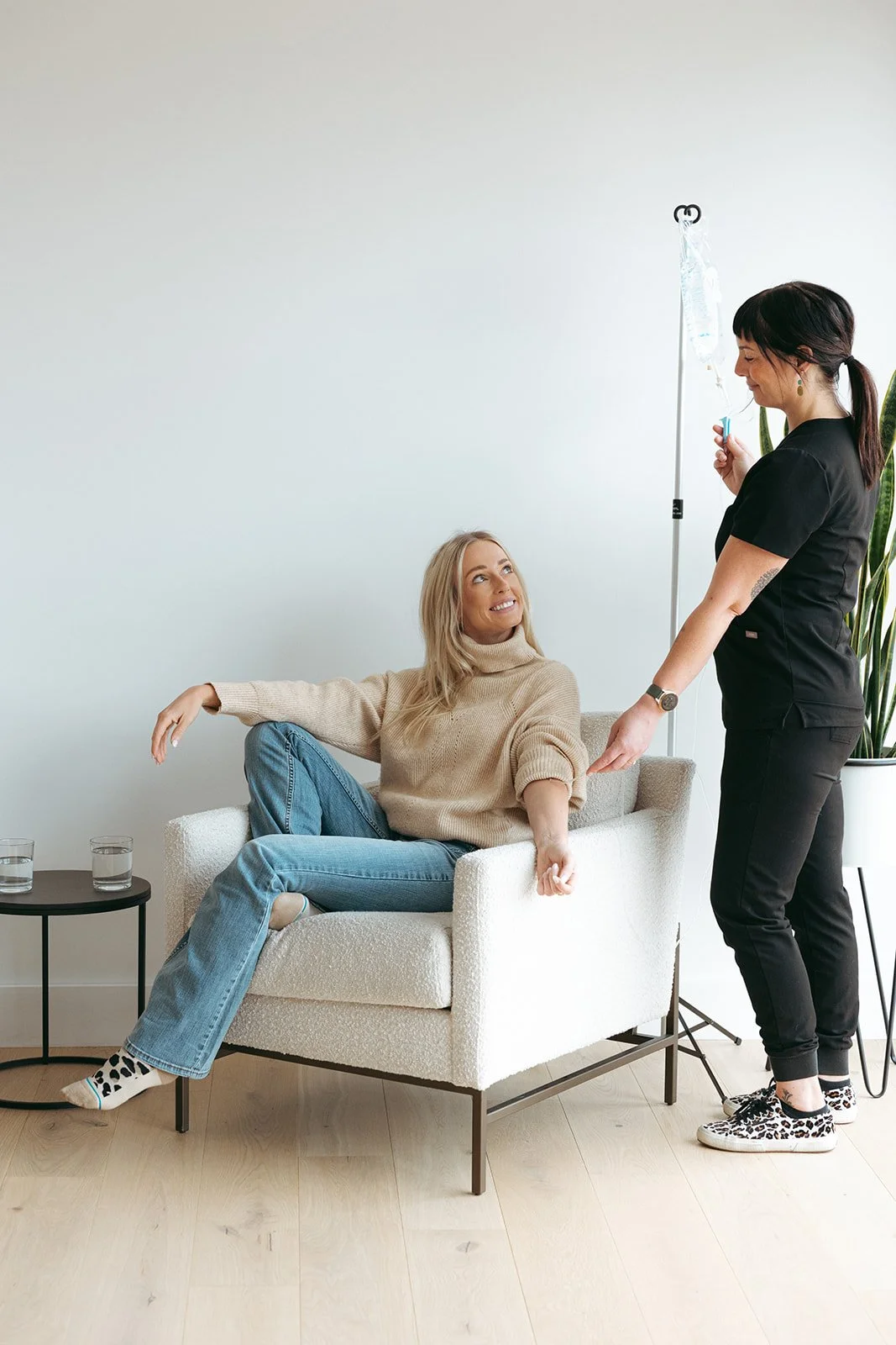 Clinician adjusting an IV drip for a smiling client seated at home during mobile IV therapy