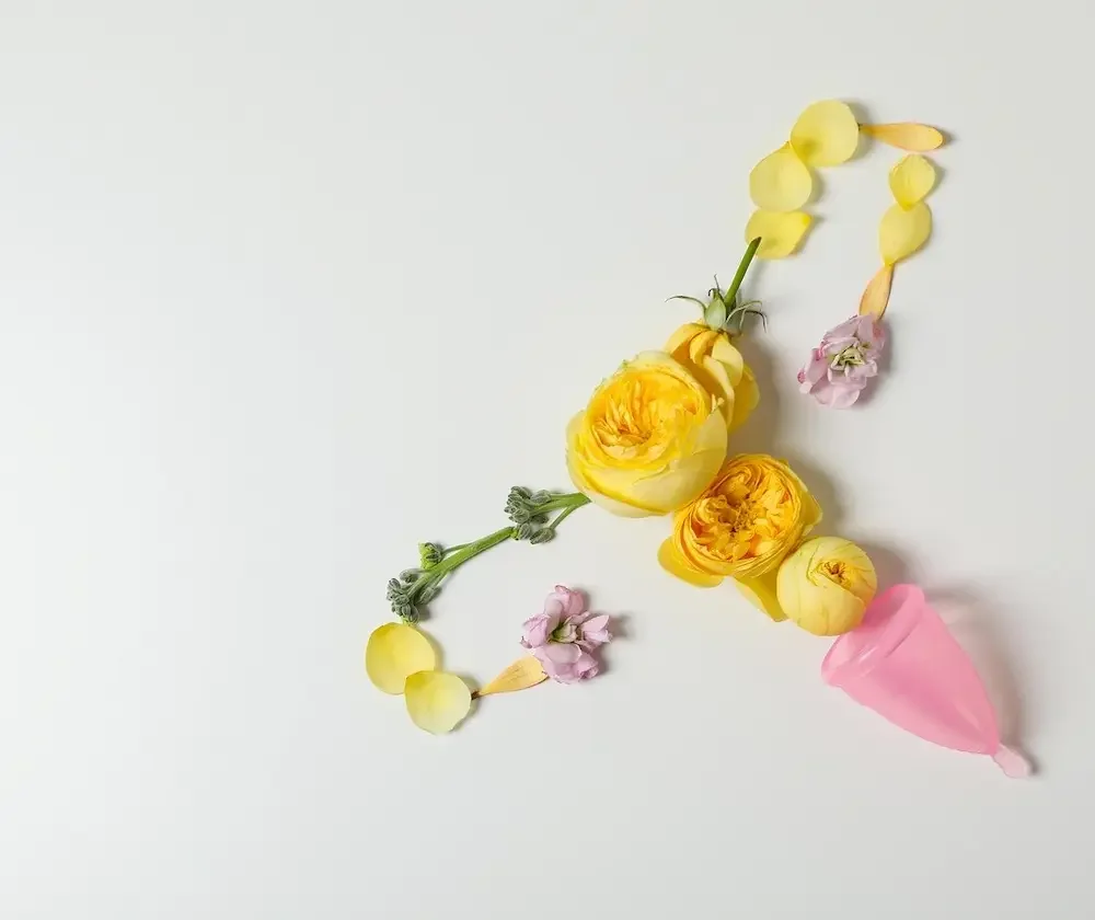 Yellow roses and petals arranged in the shape of a uterus with a menstrual cup, representing fertility and reproductive health