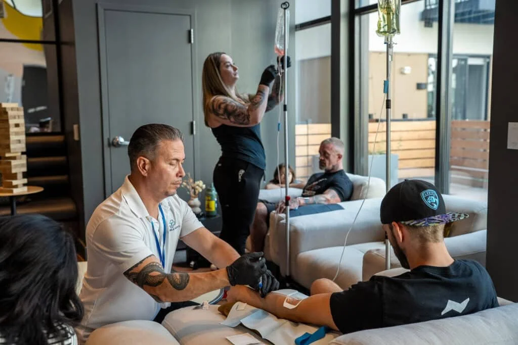 Group of men relaxing on couches while receiving IV drip therapy at a private event