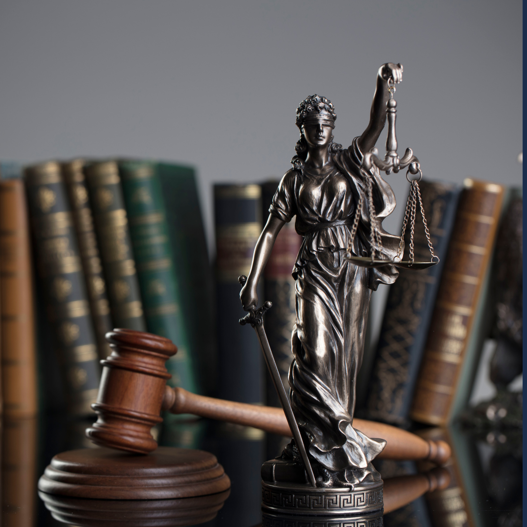 A metal statue of Lady Justice holding a set of scales, with a bookshelf of legal books in the background.