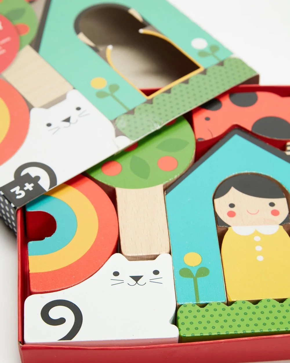Colorful wooden toy blocks featuring animals, a girl, a rainbow, trees, and a house, arranged inside a red box.