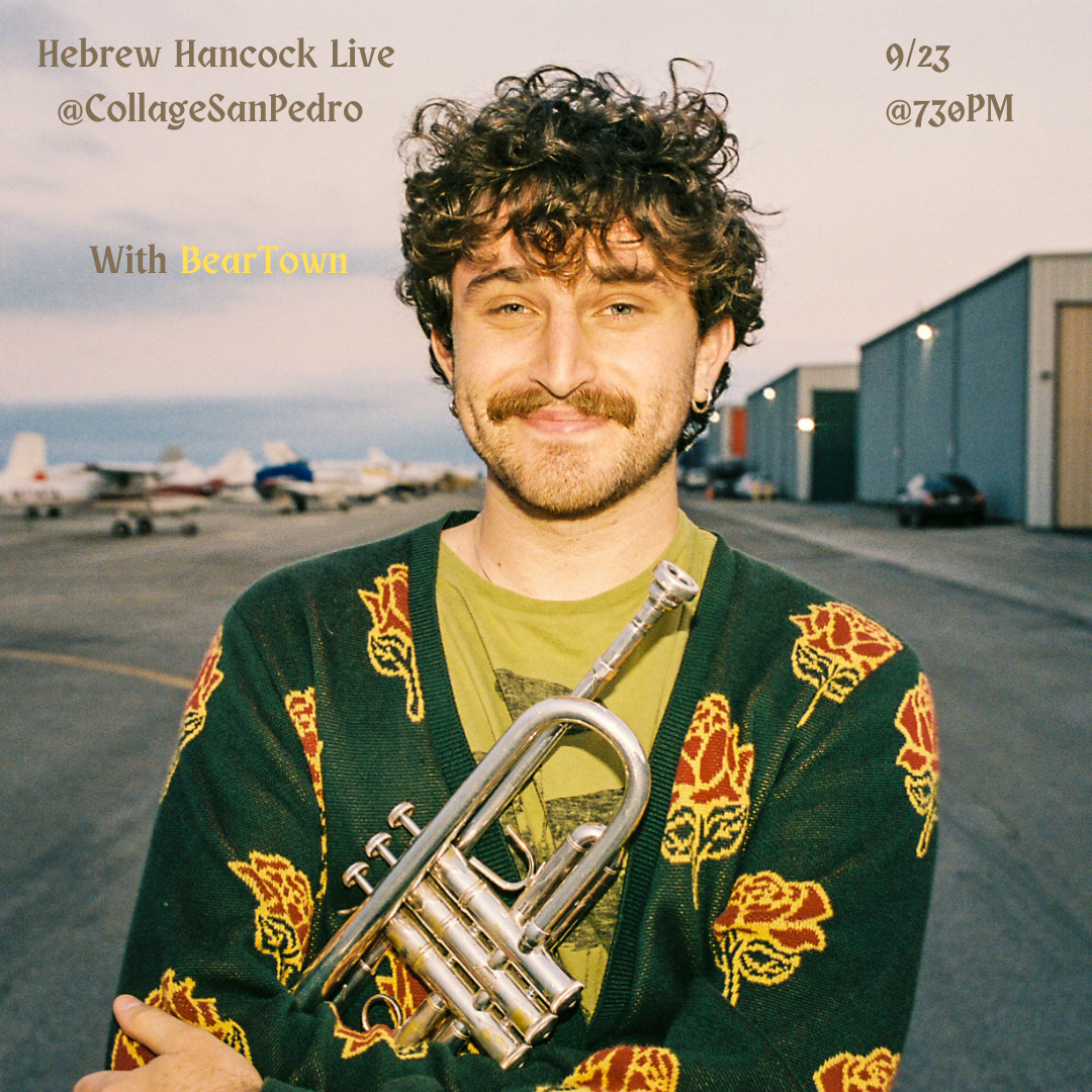 A smiling man with curly hair and a mustache, wearing a floral-patterned sweater, holding a trumpet, standing outdoors at a parking lot near hangars with small aircraft in the background.