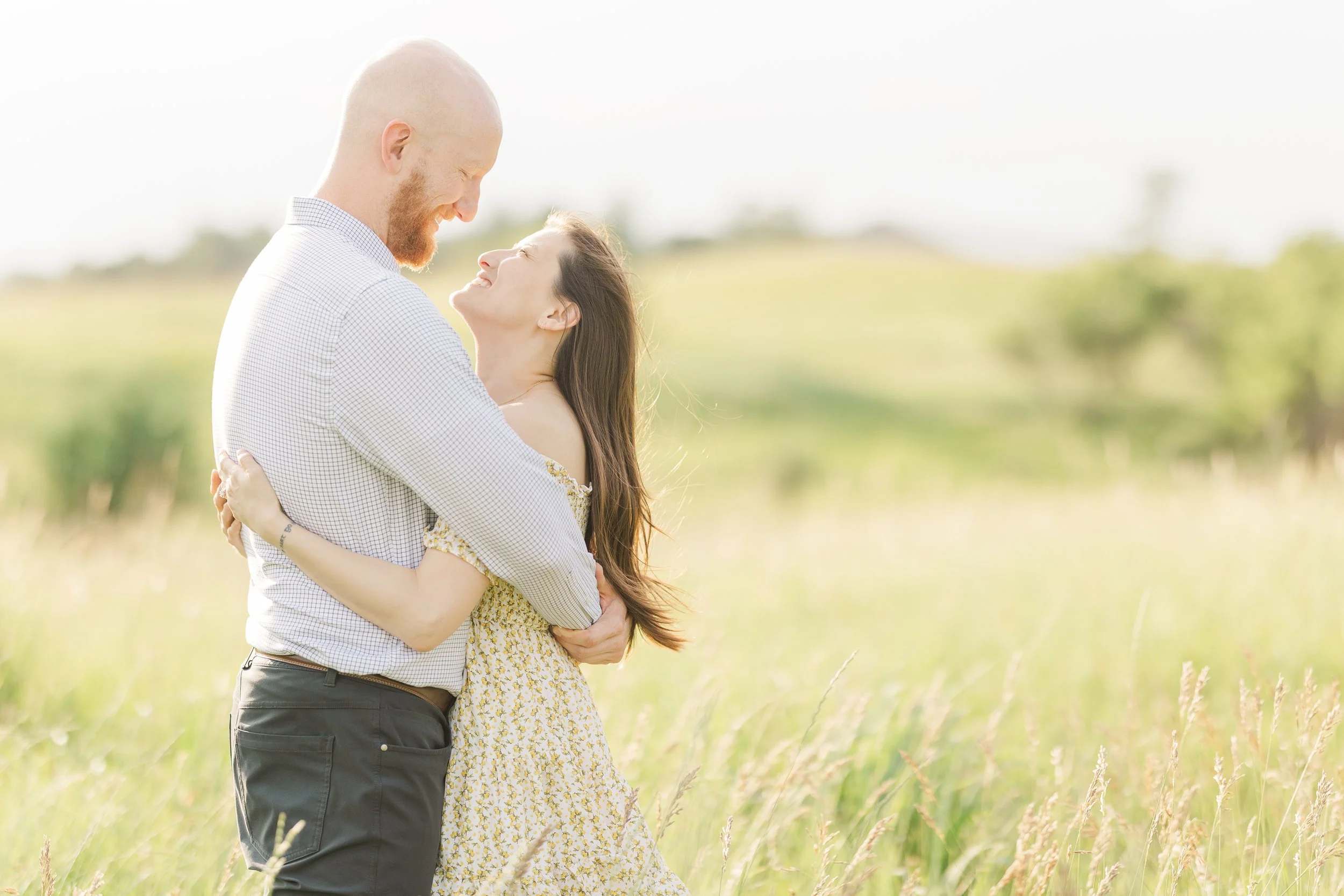 golden hour engagement session with the couple wrapping their arms around each other in a field of grass as the sunlight glows behind them