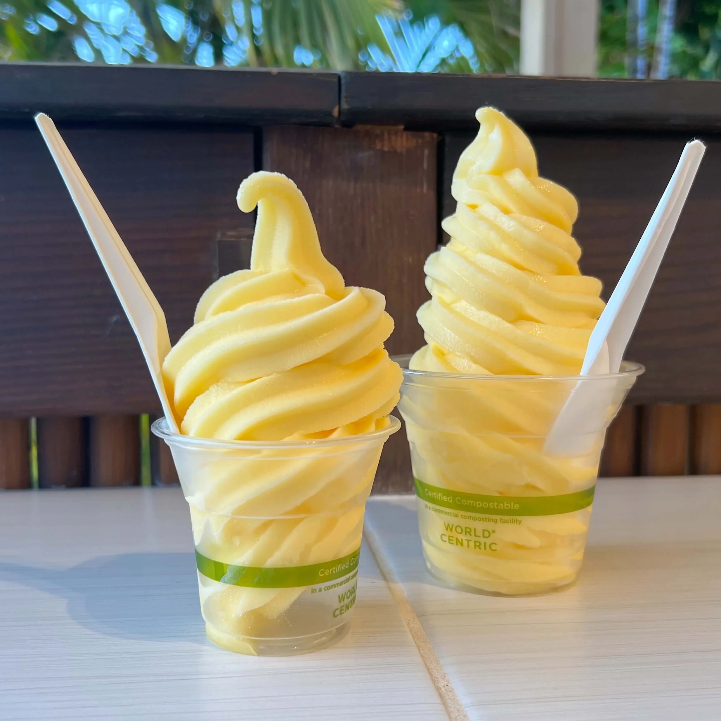 Large and small clear cups filled with yellow swirls of pineapple Dole Whip sit on the tile counter at HulaScoops in Maui.