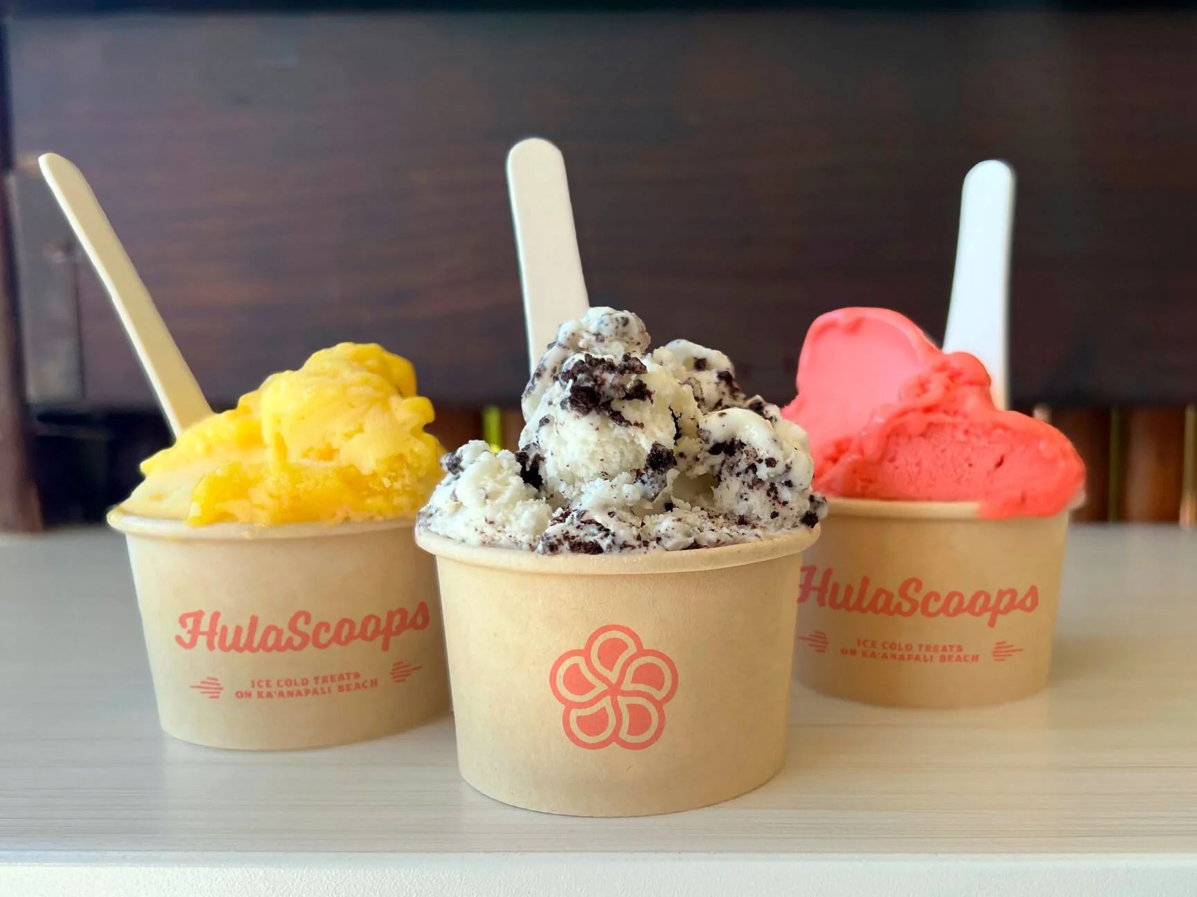 Three cups of ice cream sit on a counter at HulaScoops in Maui:  mango,  cookies and cream, and raspberry-lemon.