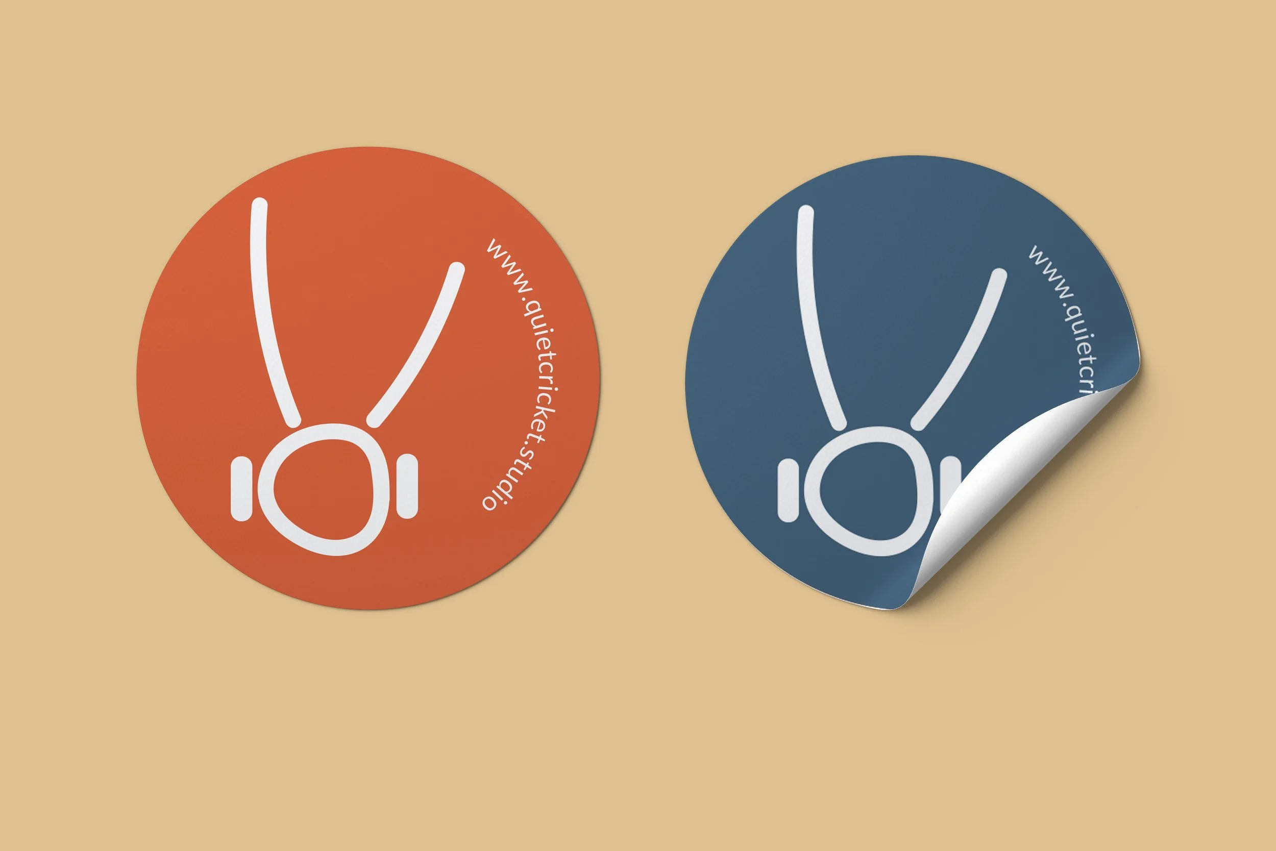 Two round stickers, one orange and one dark blue, featuring a white minimalist headphone illustration and the website URL www.quietcircle.studio, placed on a light orange background.