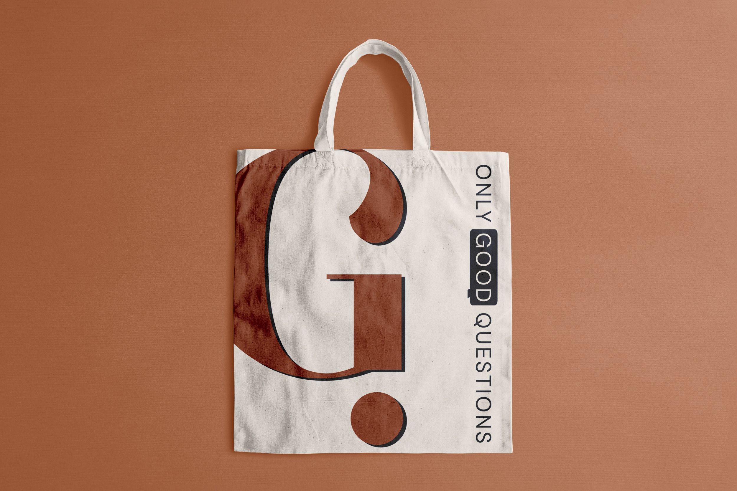 A white tote bag with a large "G". The tote has smaller text reading 'ONLY GOOD QUESTIONS' arranged vertically, with some words highlighted in navy.