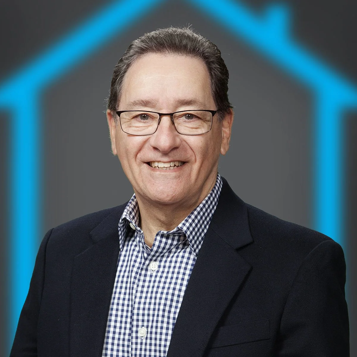 A middle-aged man with dark hair and glasses, dressed in a checkered shirt and dark blazer, smiling in front of a gray background with a blue outline of a house.