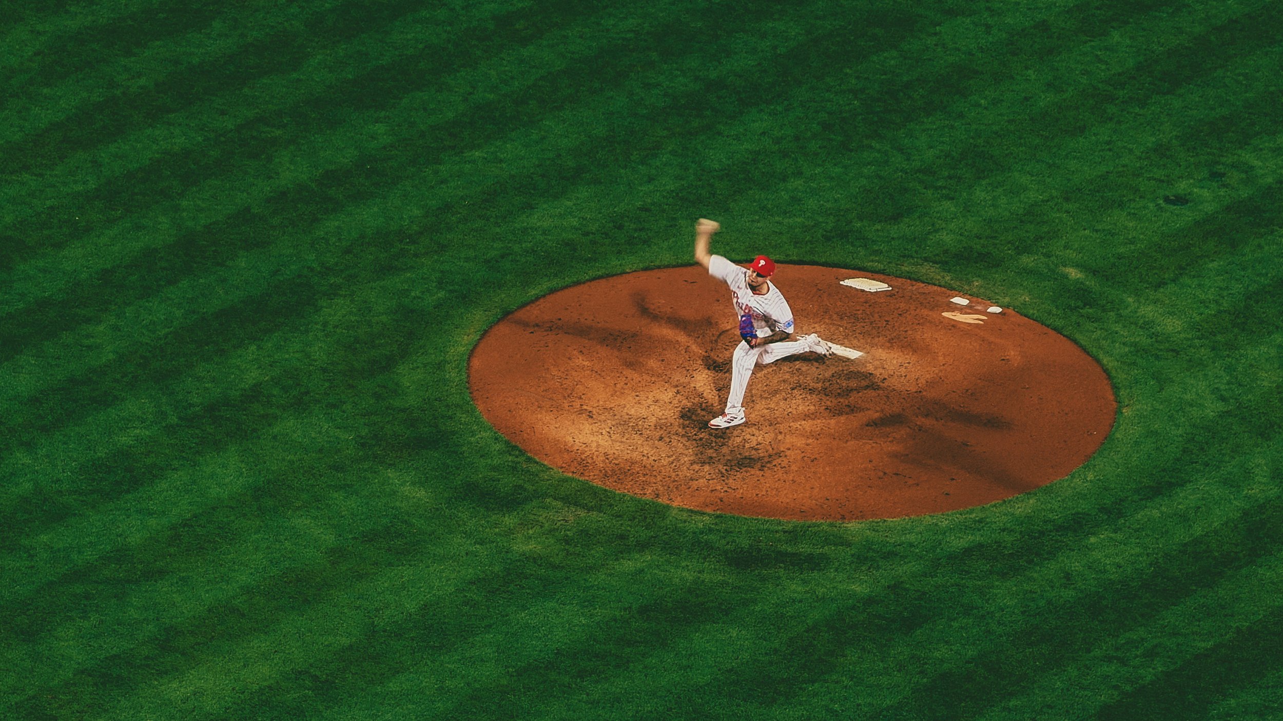 A baseball pitcher in a uniform and red cap throws a pitch on the mound at a baseball field.