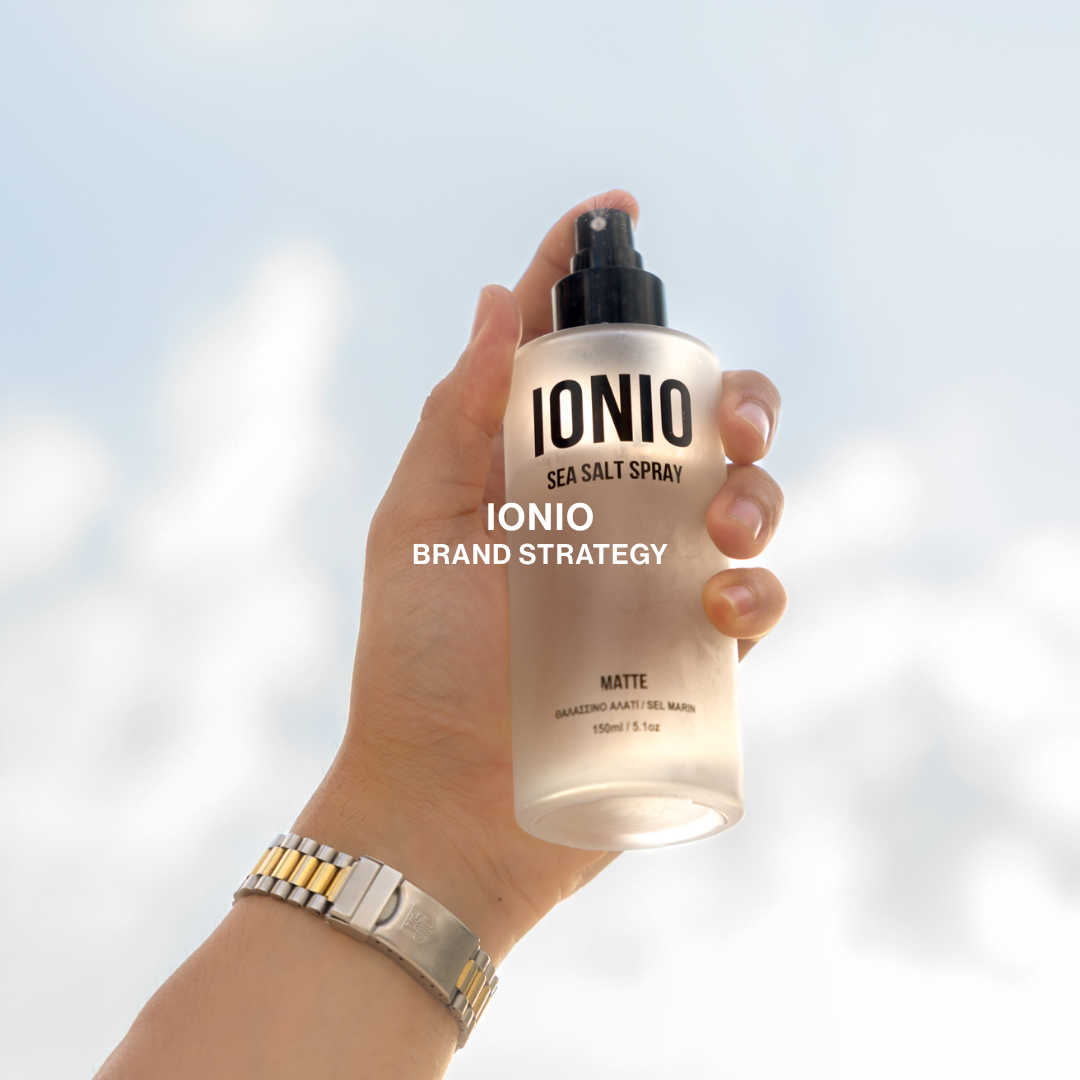 Hand holding a bottle of IONIO sea salt spray against a cloudy sky