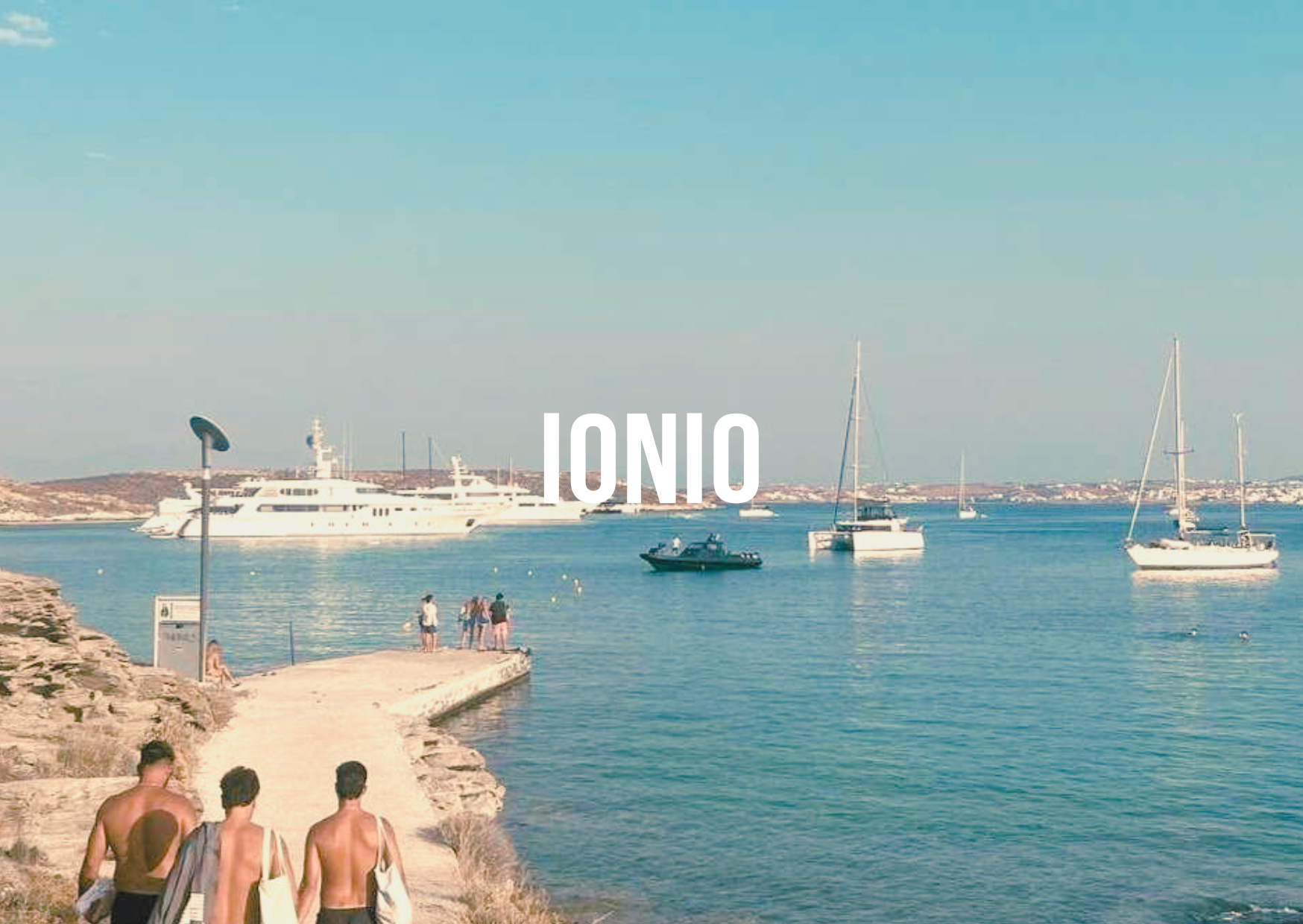 Beach scene with people walking on a path towards the ocean, yachts and sailboats in the water, and "IONIO" text overlay.