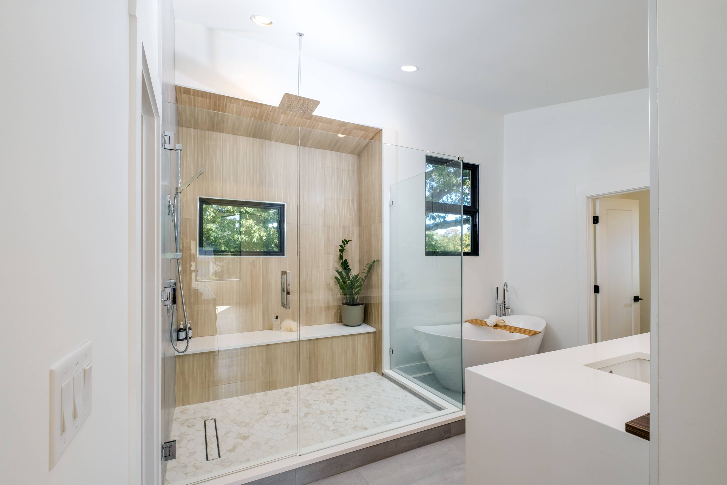 Bright, modern bathroom with glass shower enclosure, wood-look tiled shower walls, a built-in bench, and a freestanding soaking tub